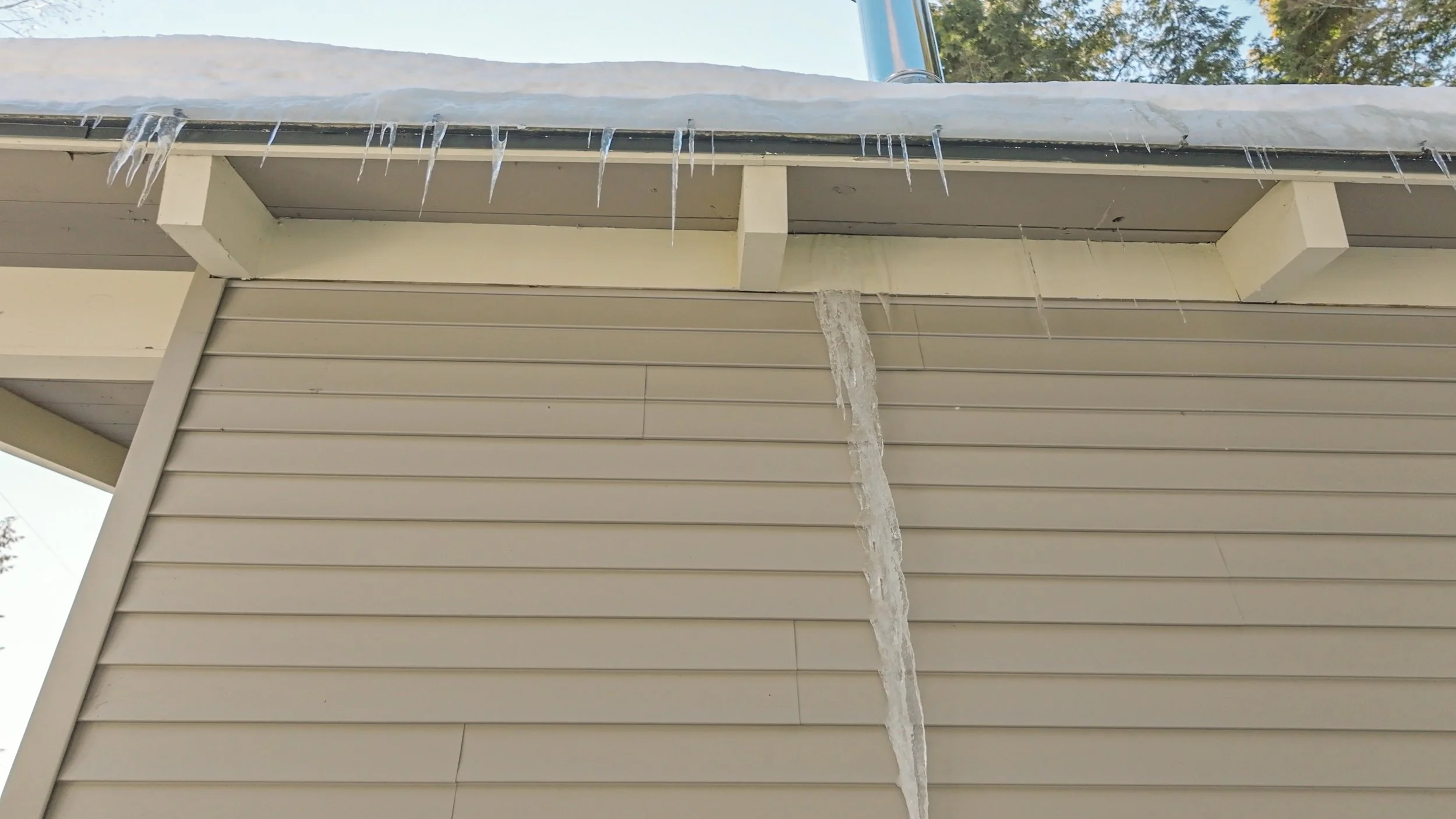 Icicles hanging from the edge of a roof above light-colored horizontal siding.
