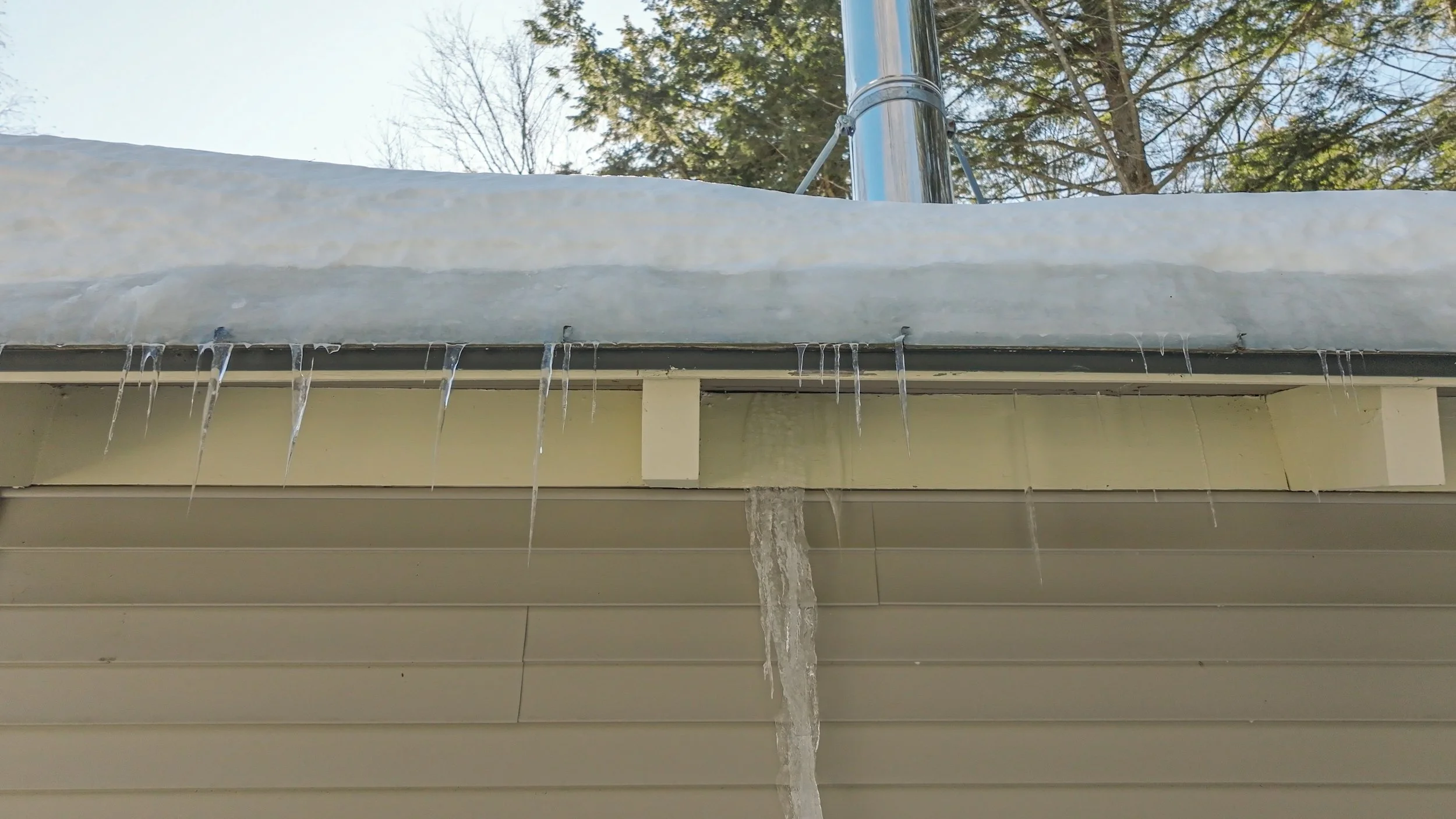 Icicles hanging from the edge of a roof with melting snow and a cloudy sky in the background.