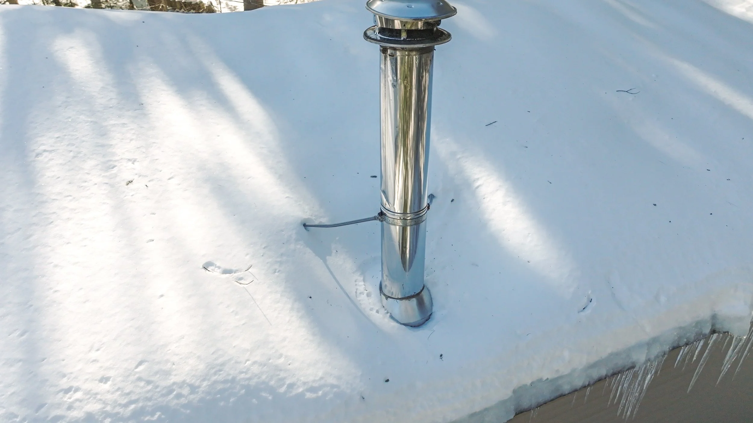 A metal pole on a snow-covered surface with icicles hanging from the edge.