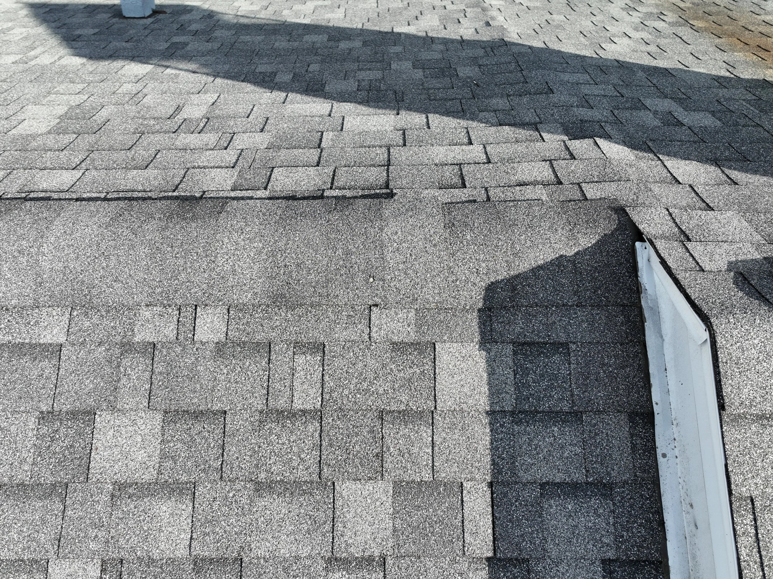 Close-up of a roof with asphalt shingles, showing a patch where some shingles are missing or damaged, exposing the underlying structure.