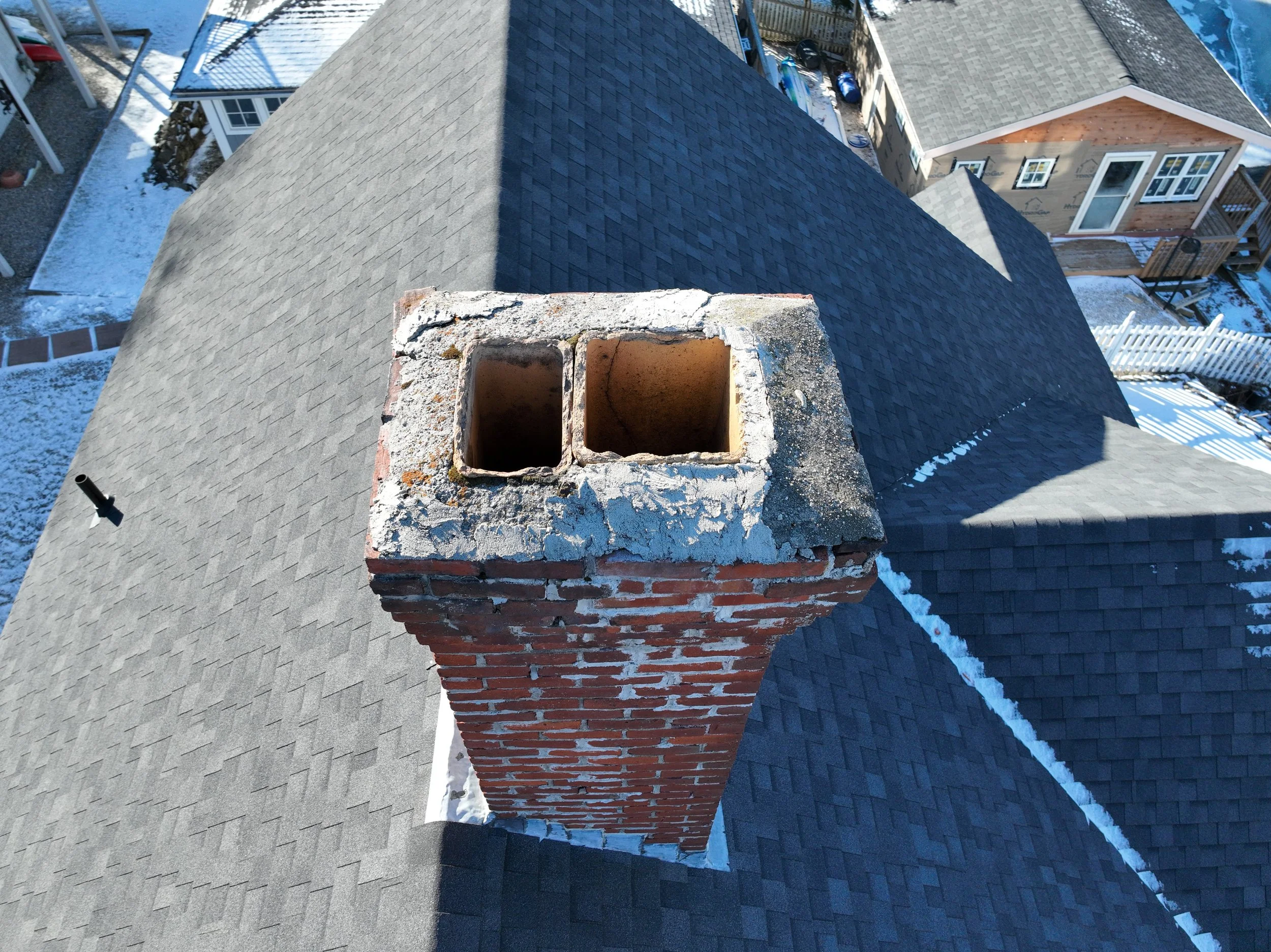 A rooftop chimney with two openings, made of red bricks with a concrete cap, seen from above during winter.