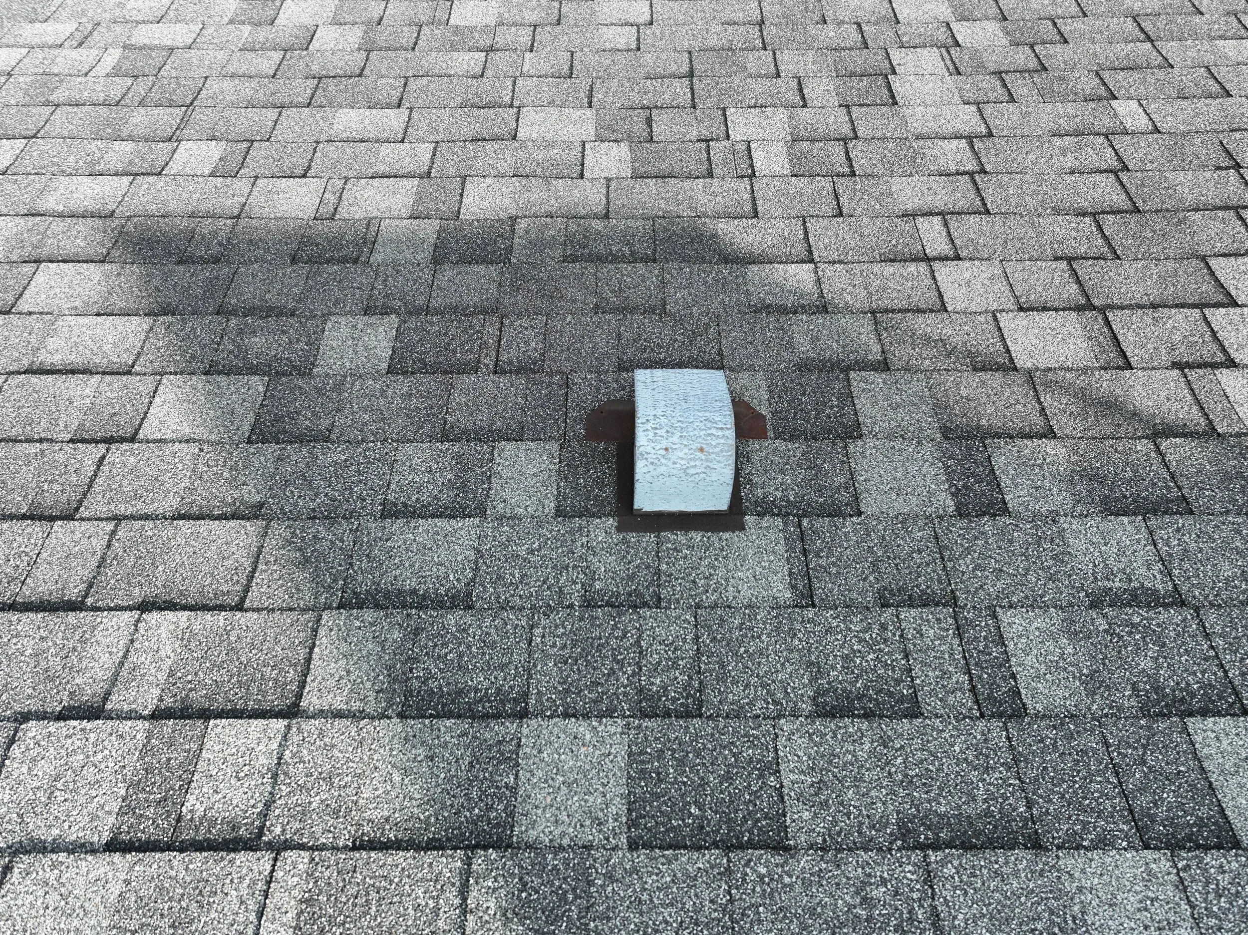Close-up of a gray asphalt shingle roof with a vent pipe in the center.