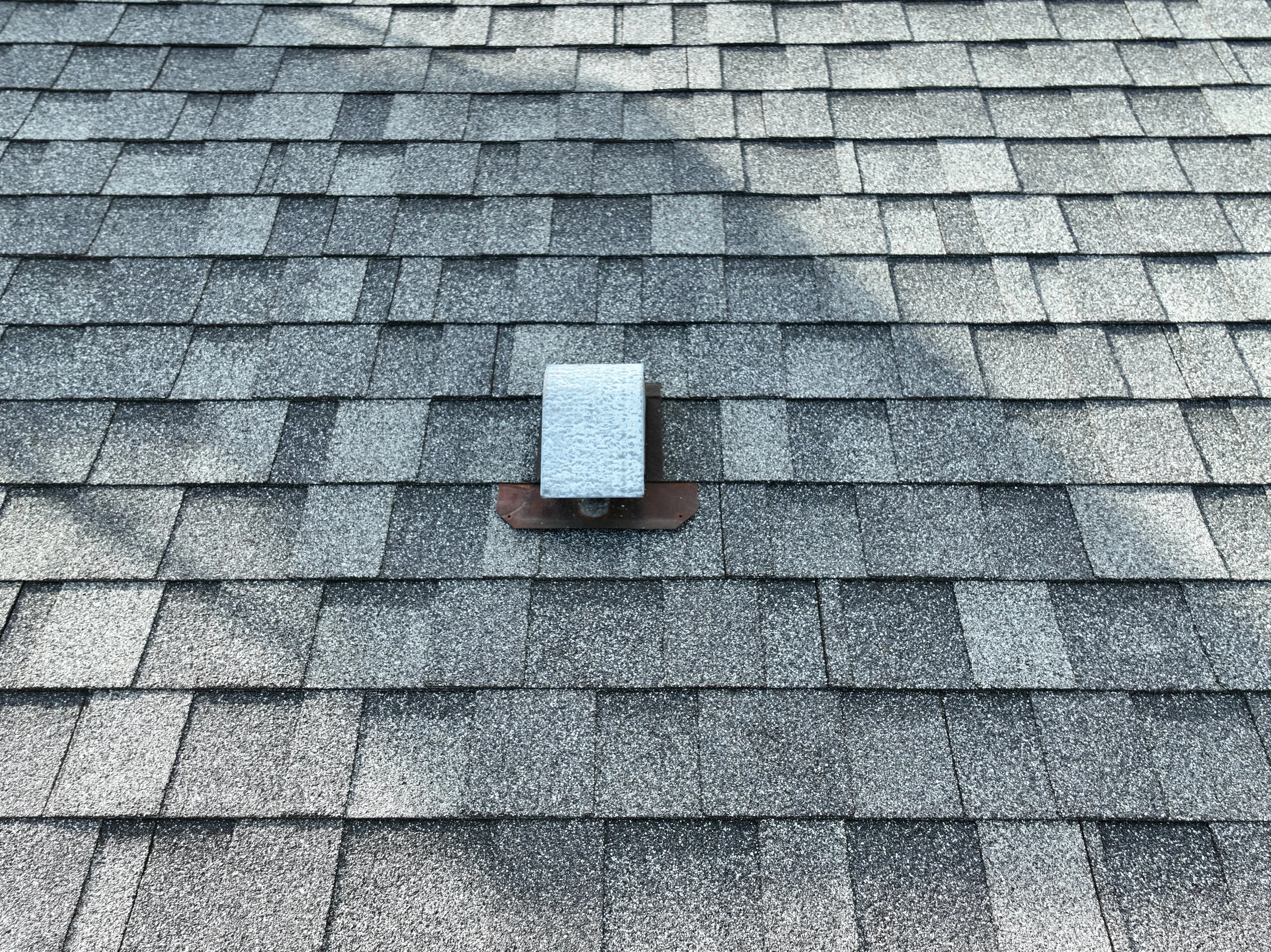 Close-up of a roof with asphalt shingles and a metal vent pipe with a protective cap.