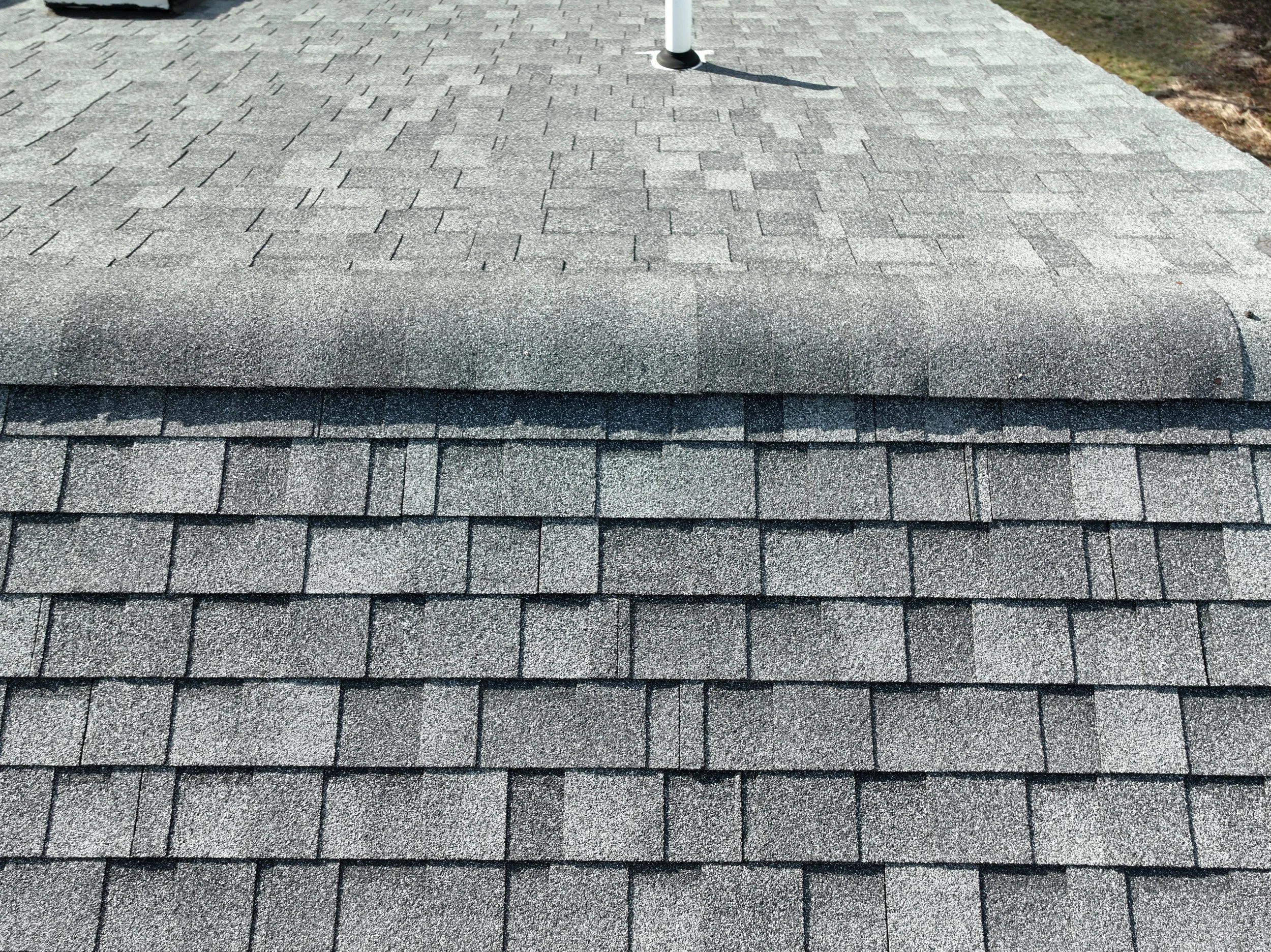 Close-up view of a roof with asphalt shingles, showing different sections with layered shingles in shades of gray.