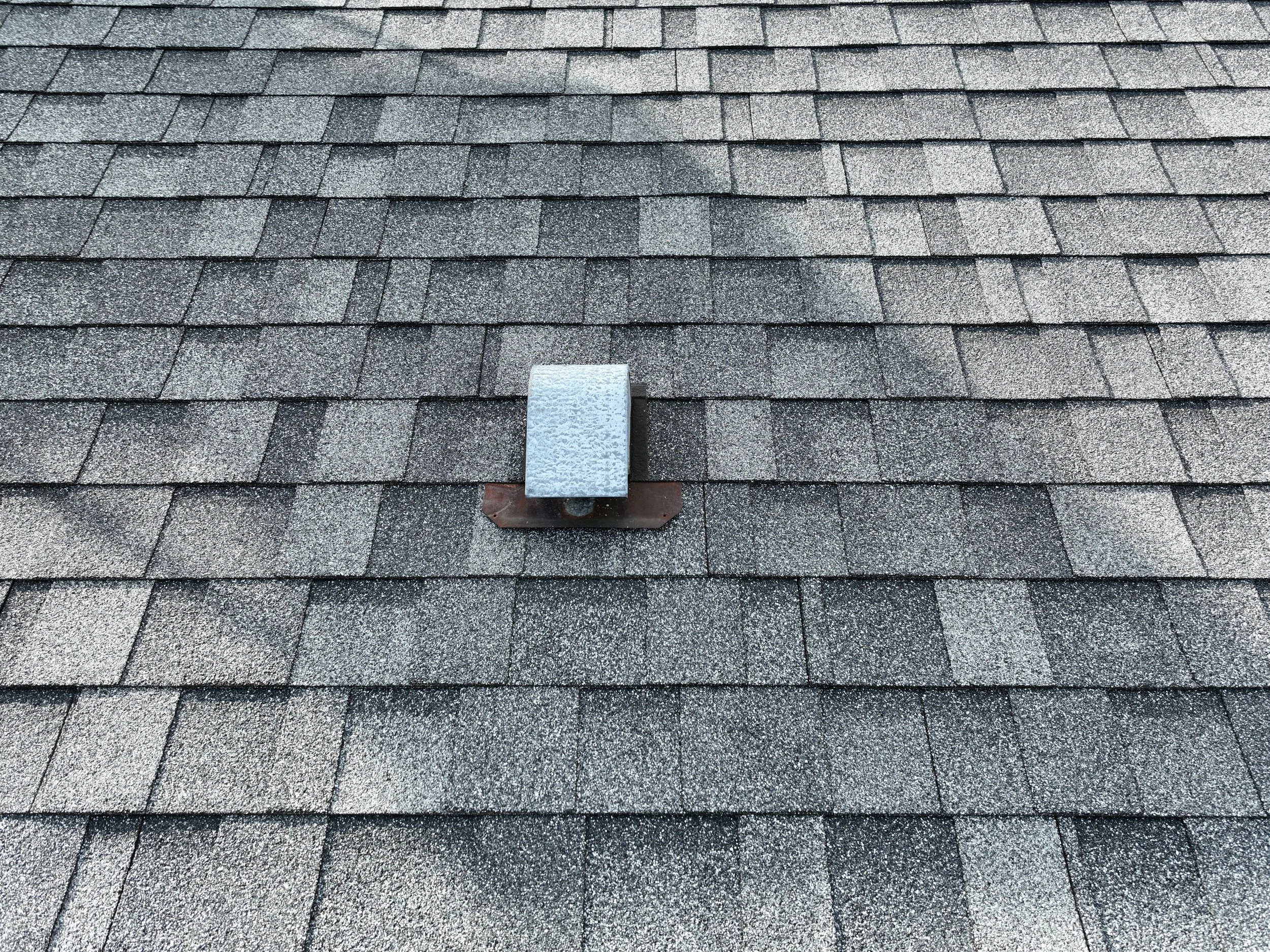 Close-up view of asphalt shingles on a roof with a metal vent cap in the center.