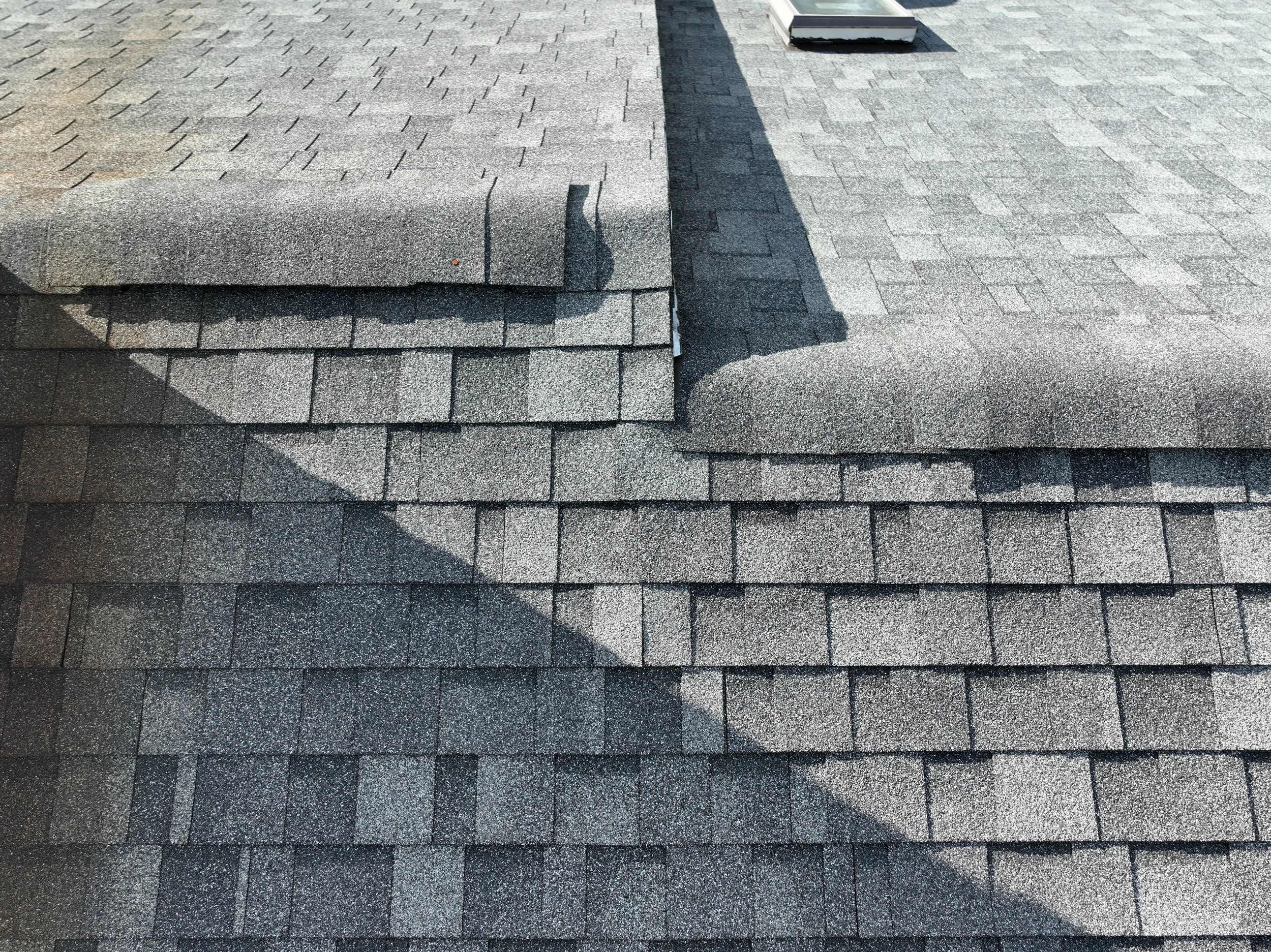 Close-up of a roof with asphalt shingles and vent pipe, showing multiple layers and shadow cast on the shingles.