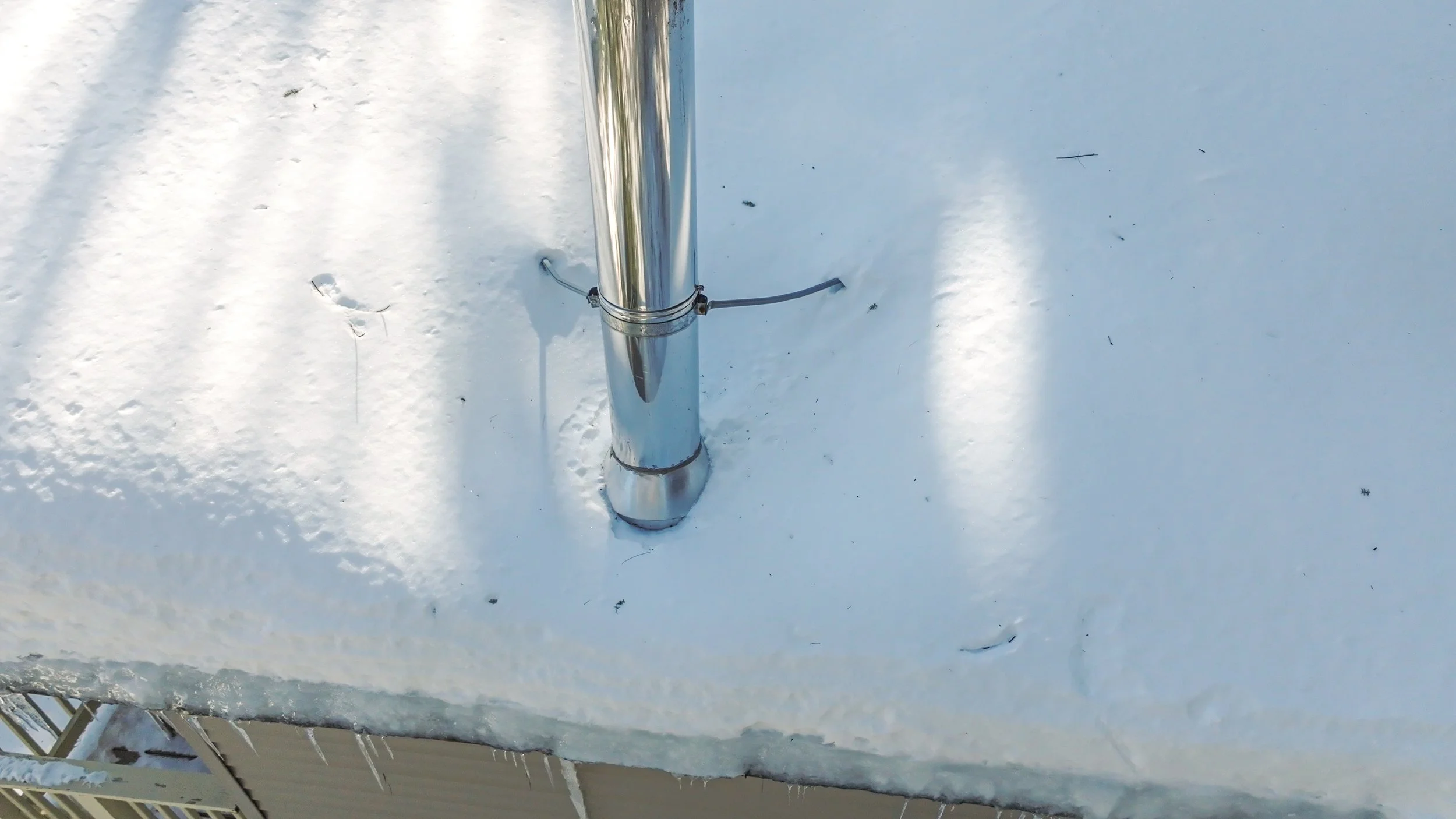 Close-up of a metal pole on a snow-covered rooftop with visible ice and snow along the edge.