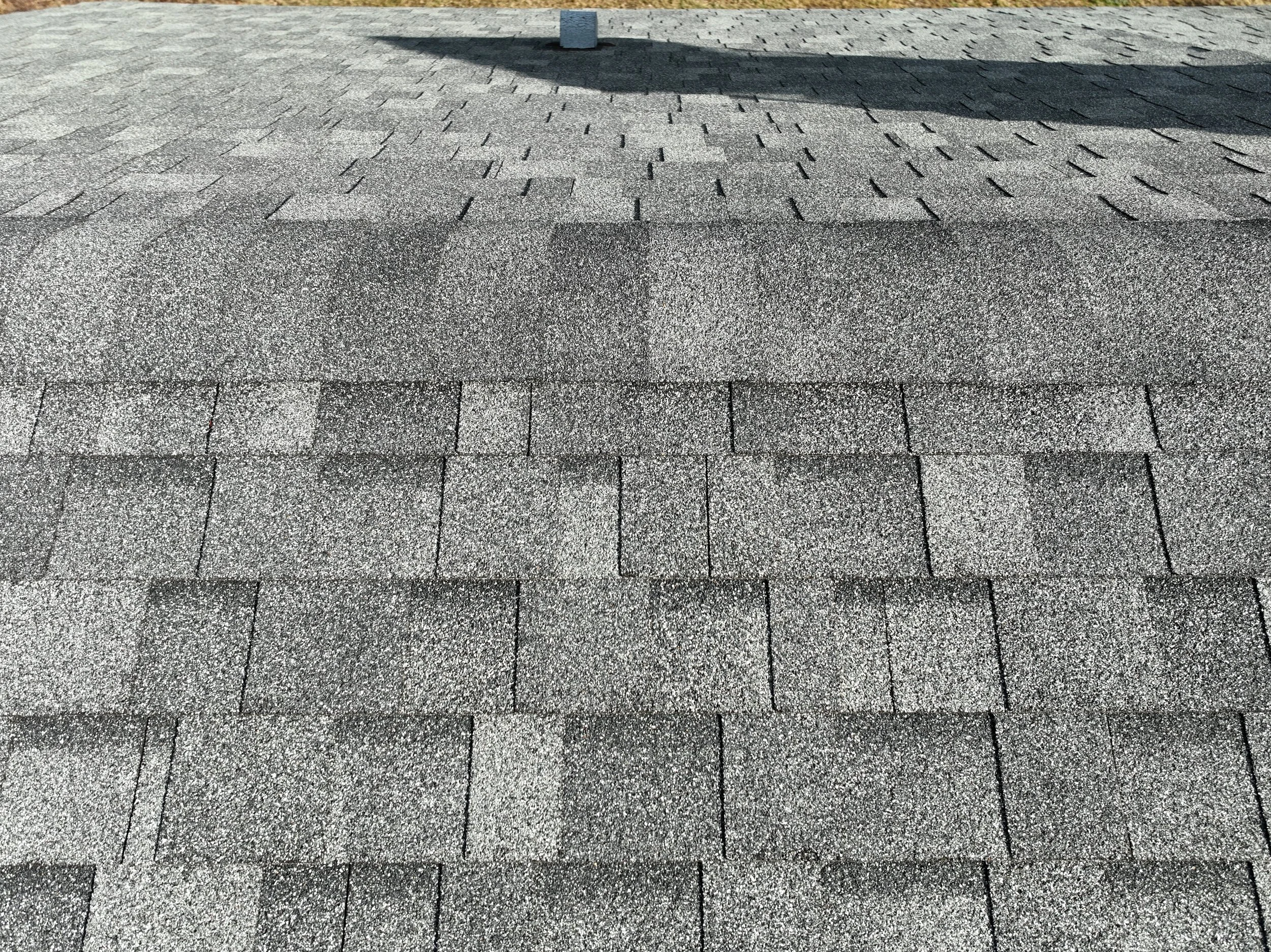 Close-up of a shingled roof with asphalt shingles in different shades of gray and some shadowing.