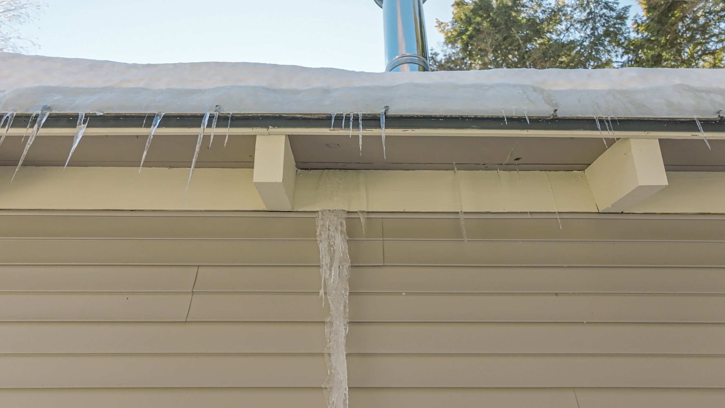 Icicles formed on the edge of a roof, with a long icicle hanging down, and some ice melting.