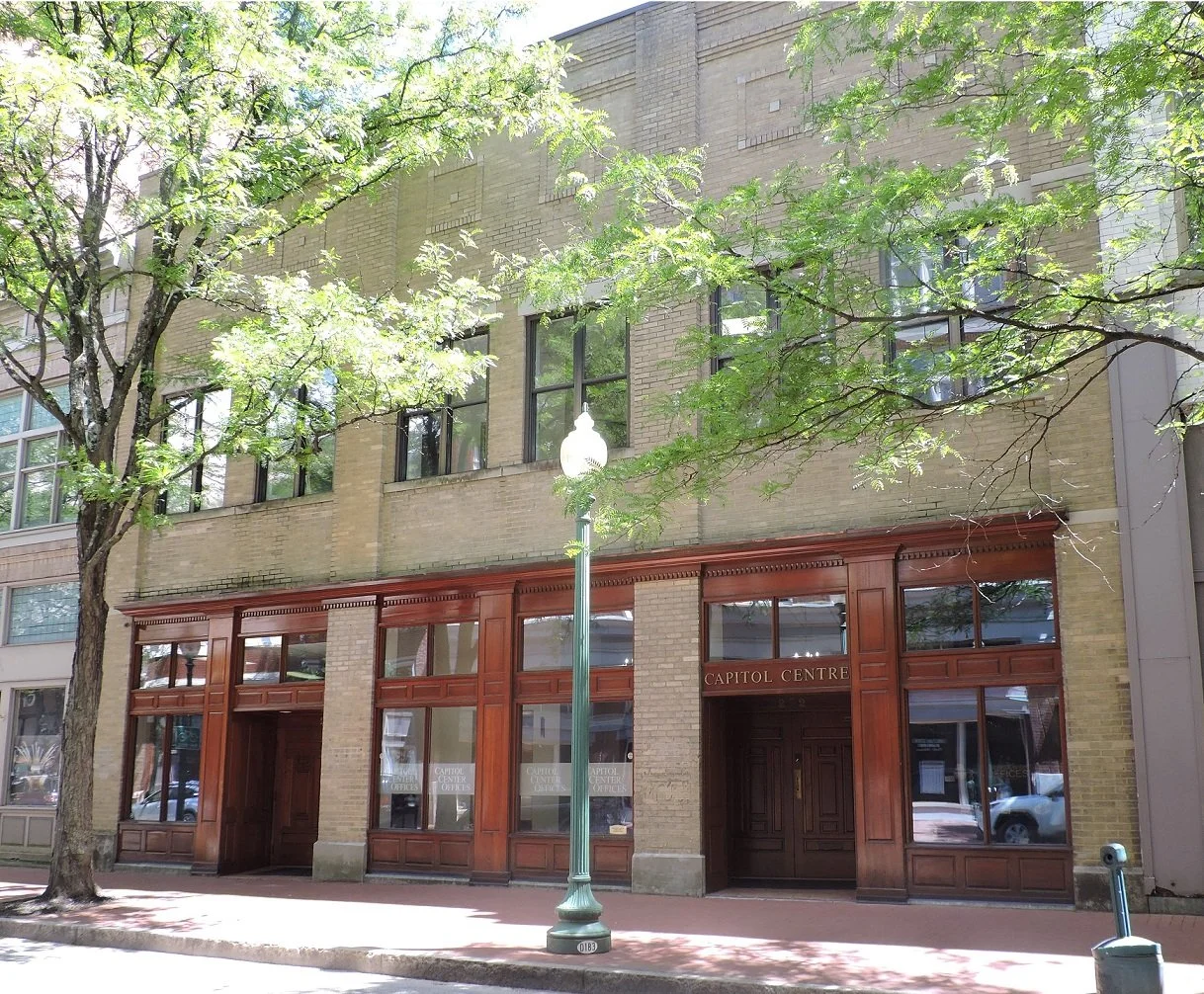Front view of the Capitol Centre, a building with a brick facade and wooden trim, with trees and a lamppost on the sidewalk in front.