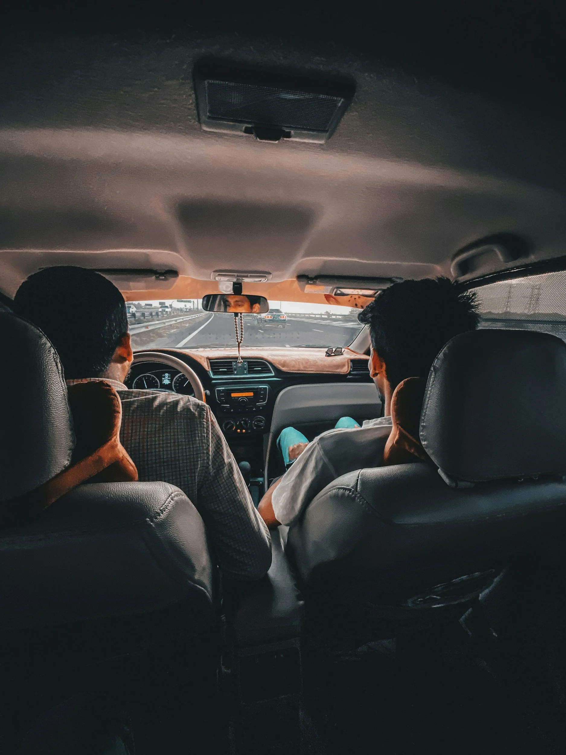Two men driving together in a sedan on a highway.