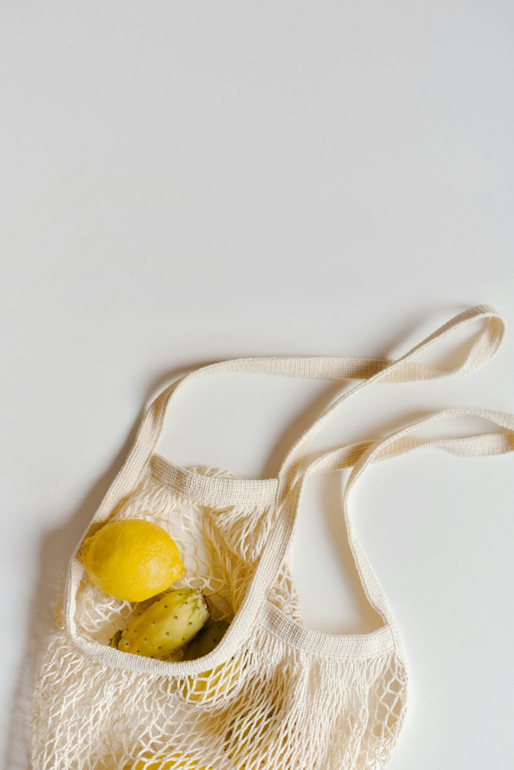 A mesh shopping bag containing a lemon and a prickly pear fruit, placed on a white surface.