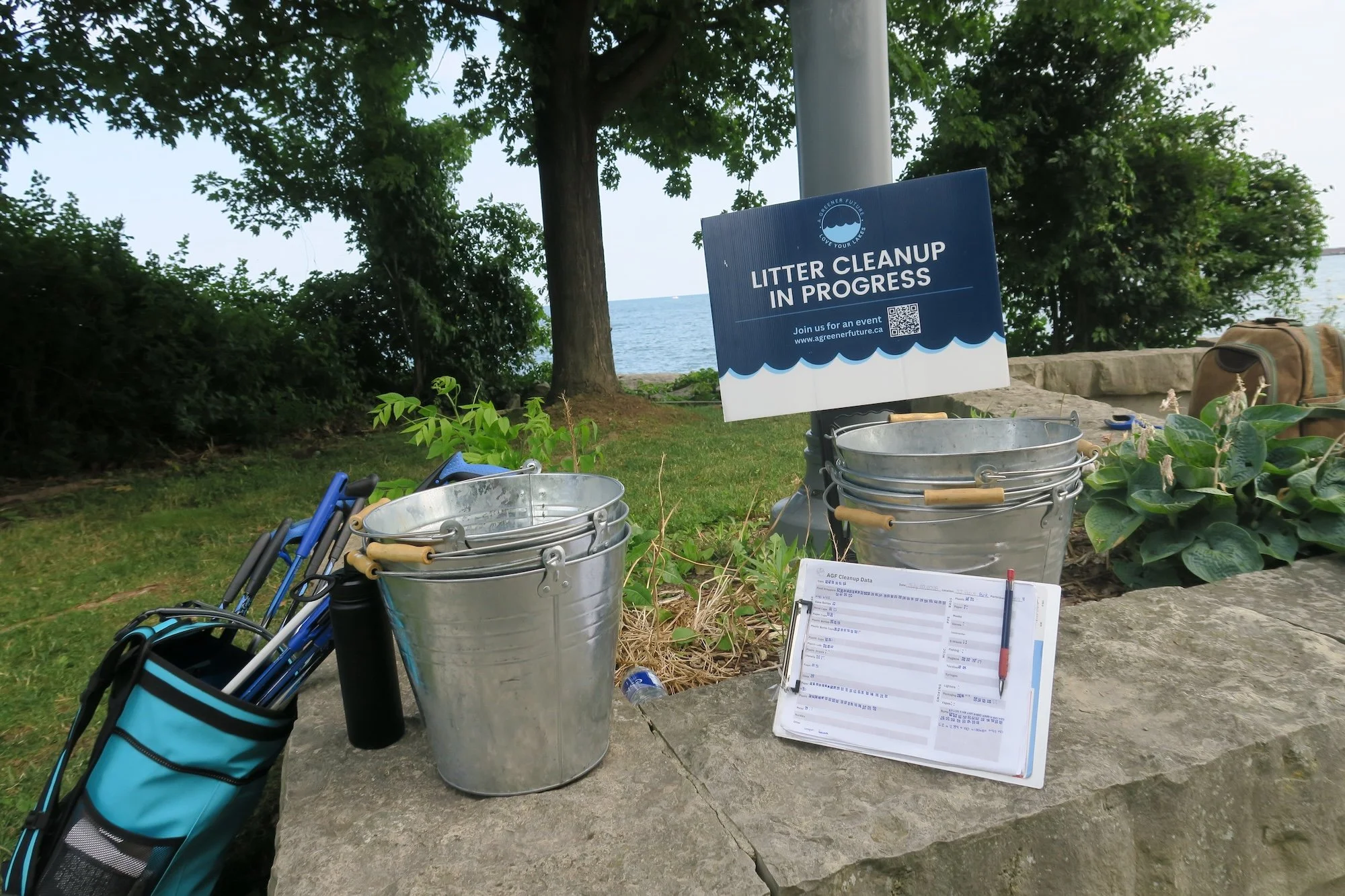 Litter cleanup equipment including metal buckets, a clip board with data sheets, litter pickers and a "Litter Cleanup in Progress" sign