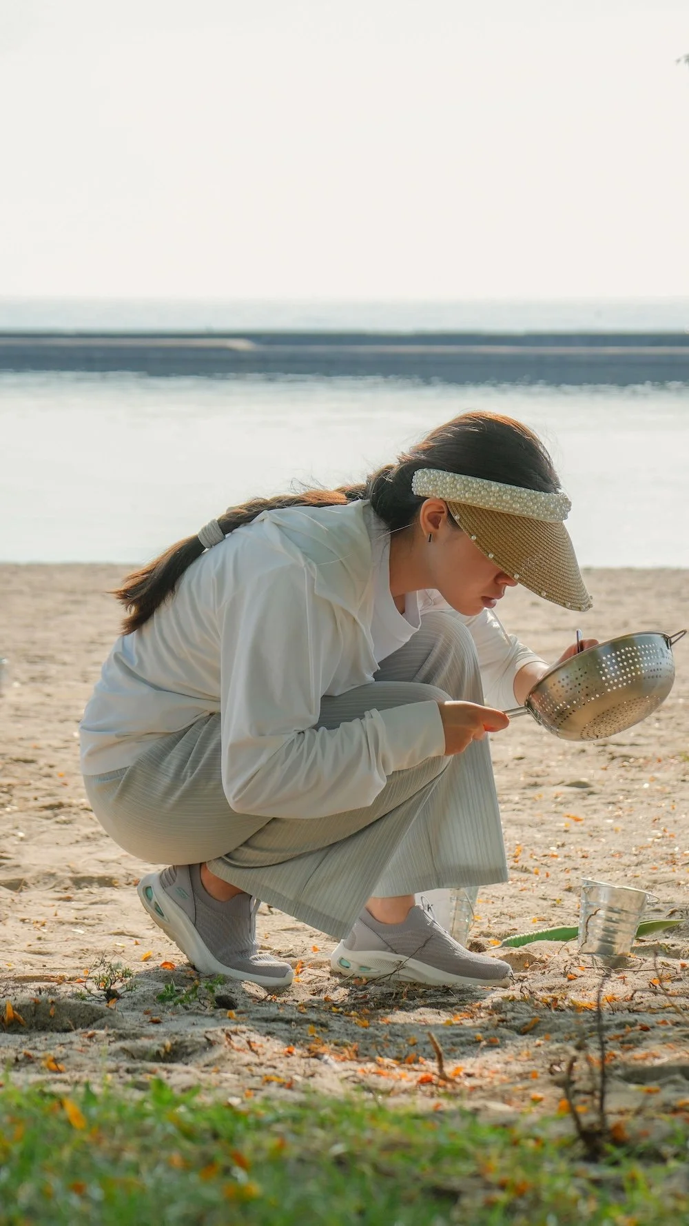 Woman nurdle hunting on the beach with a sifter on the sand.