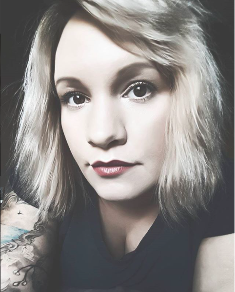 Black and white close-up portrait of a young woman with shoulder-length hair and a tattoo on her shoulder.