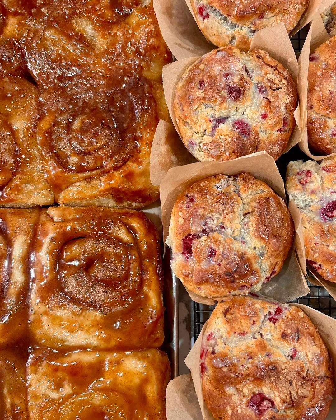 Close-up of cinnamon rolls with icing on the left and cranberry muffins in paper liners on the right.