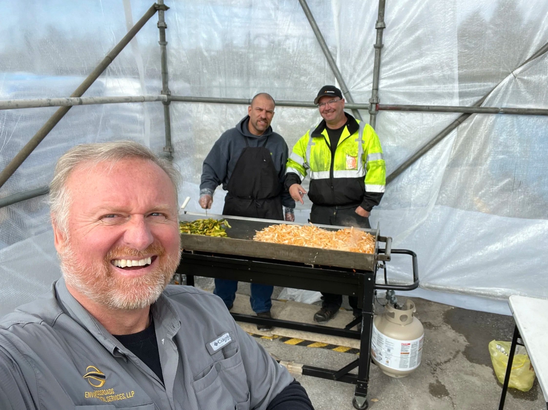 A smiling woman with glasses and curly hair, wearing a striped shirt and layered necklaces.