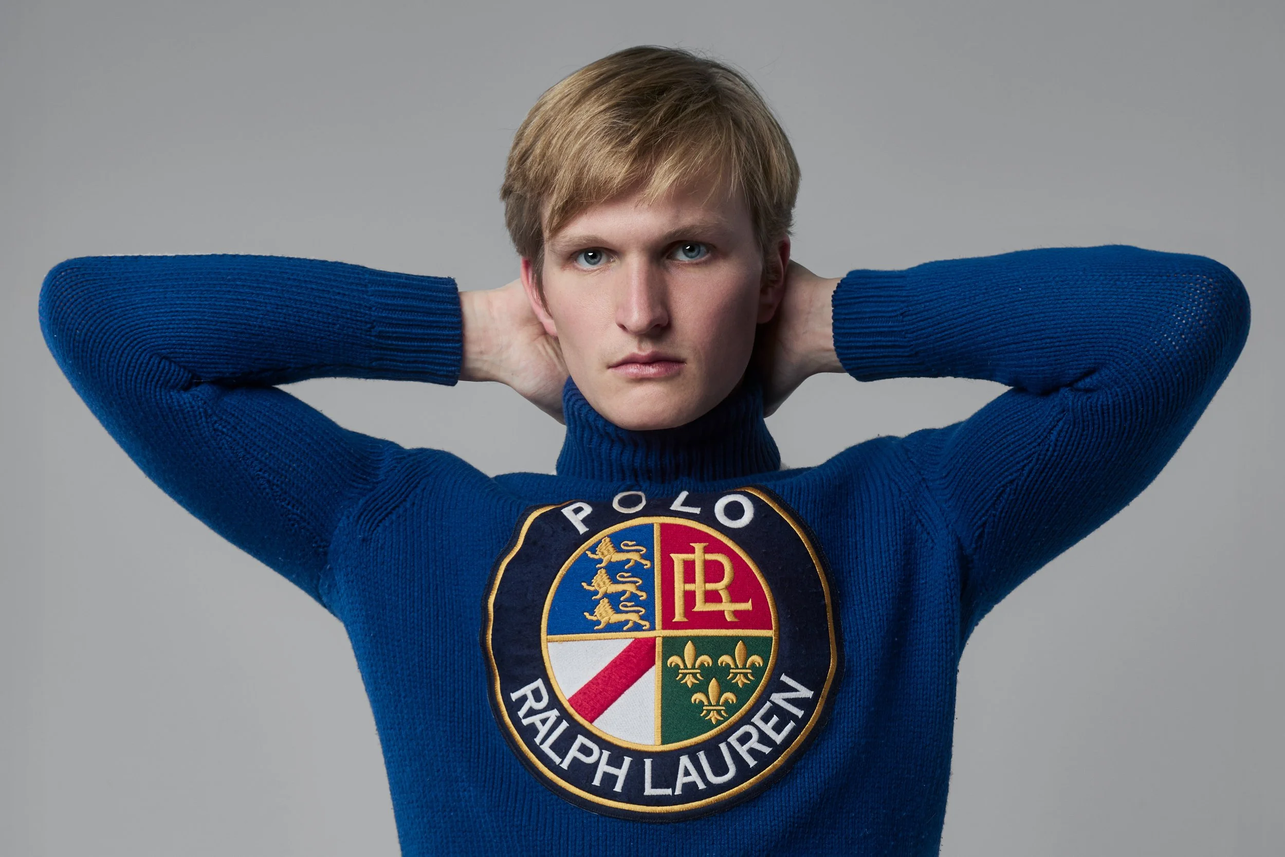 A young man with blonde hair, wearing a blue sweater with the Ralph Lauren Polo logo.