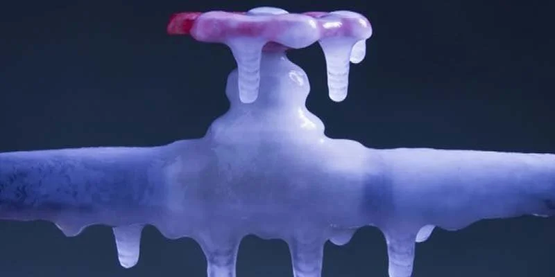 Close-up of frozen valve and pipe with ice on it and a dark background.
