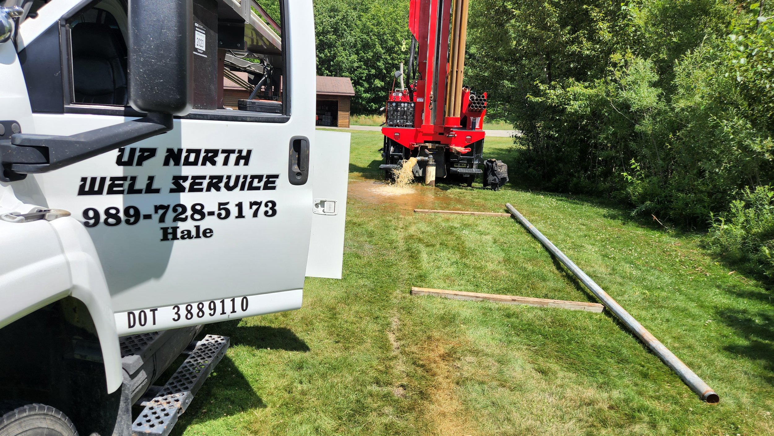 Well service truck and drilling rig in a grassy area