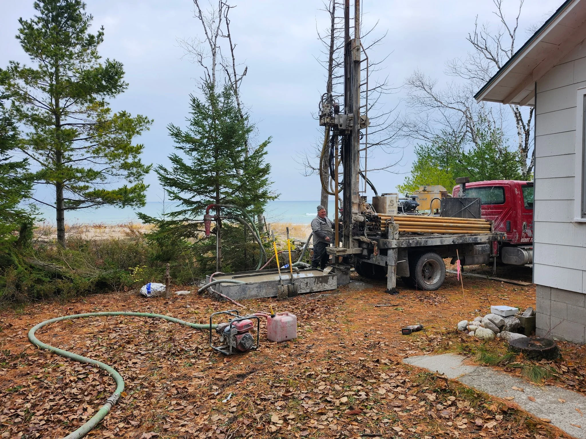 A large drilling rig is outdoors among trees with green leaves and a cloudy blue sky in the background.