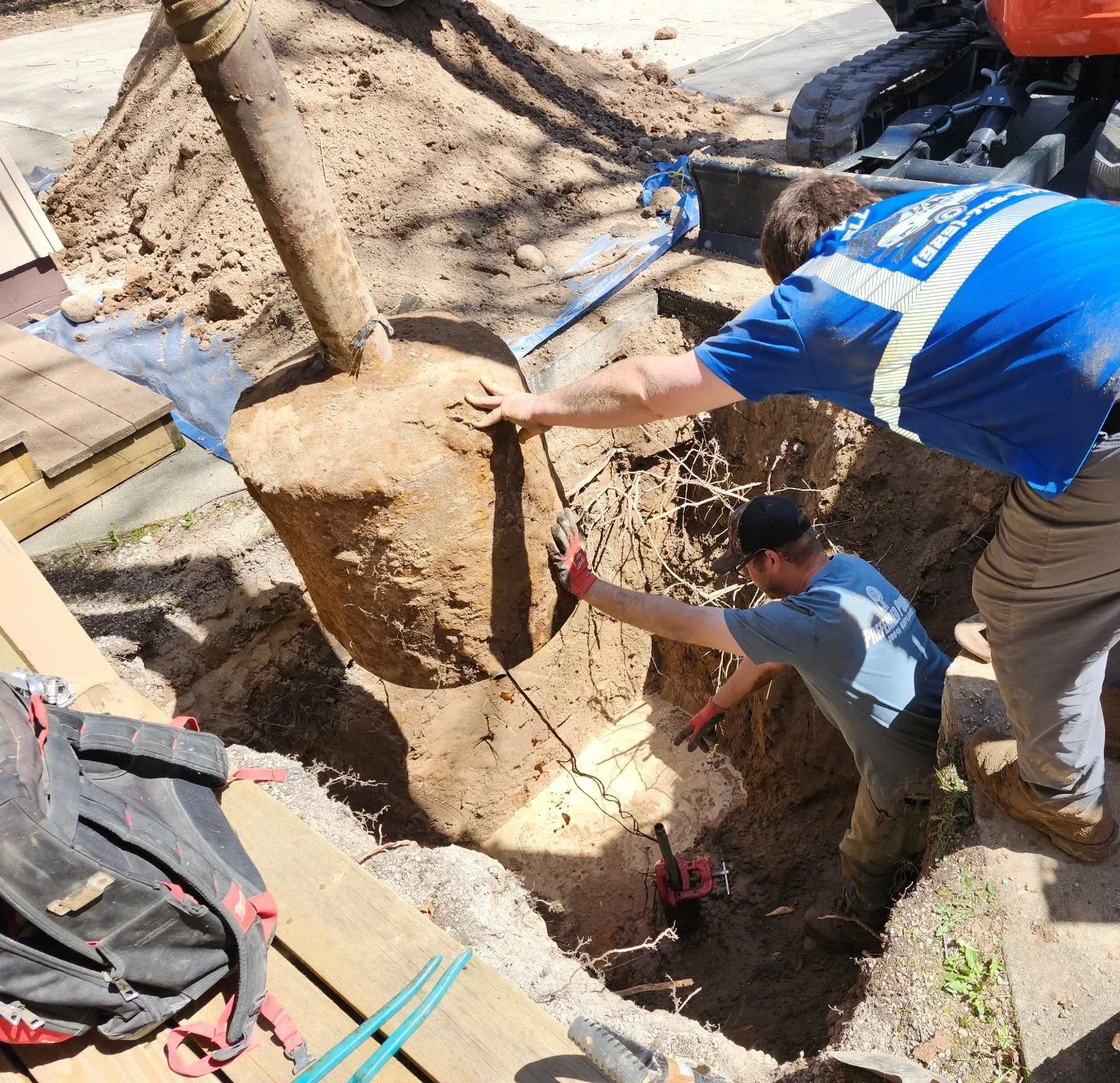 Two workers are excavating and removing a white water tank, with a excavator nearby.