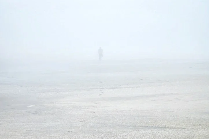A person walking in a foggy, desolate landscape with limited visibility.