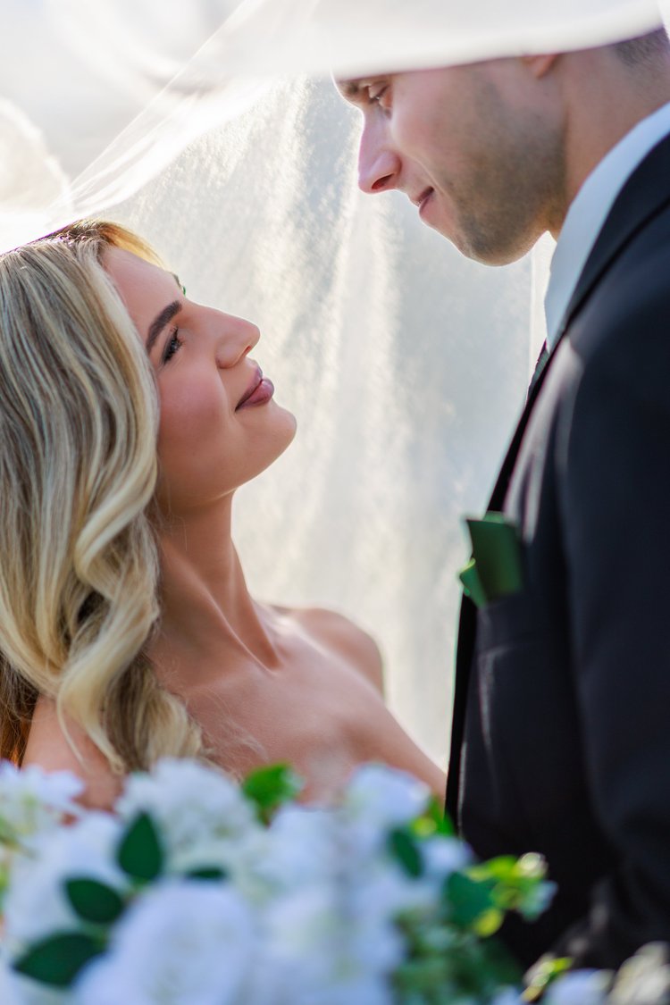 A close-up of a bride and groom looking at each other on their wedding day, with the bride holding a bouquet of white flowers.