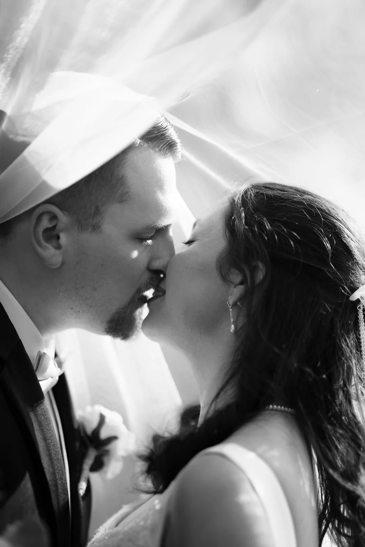 A black and white photograph of a bride and groom about to kiss, her veil framing both of their faces.