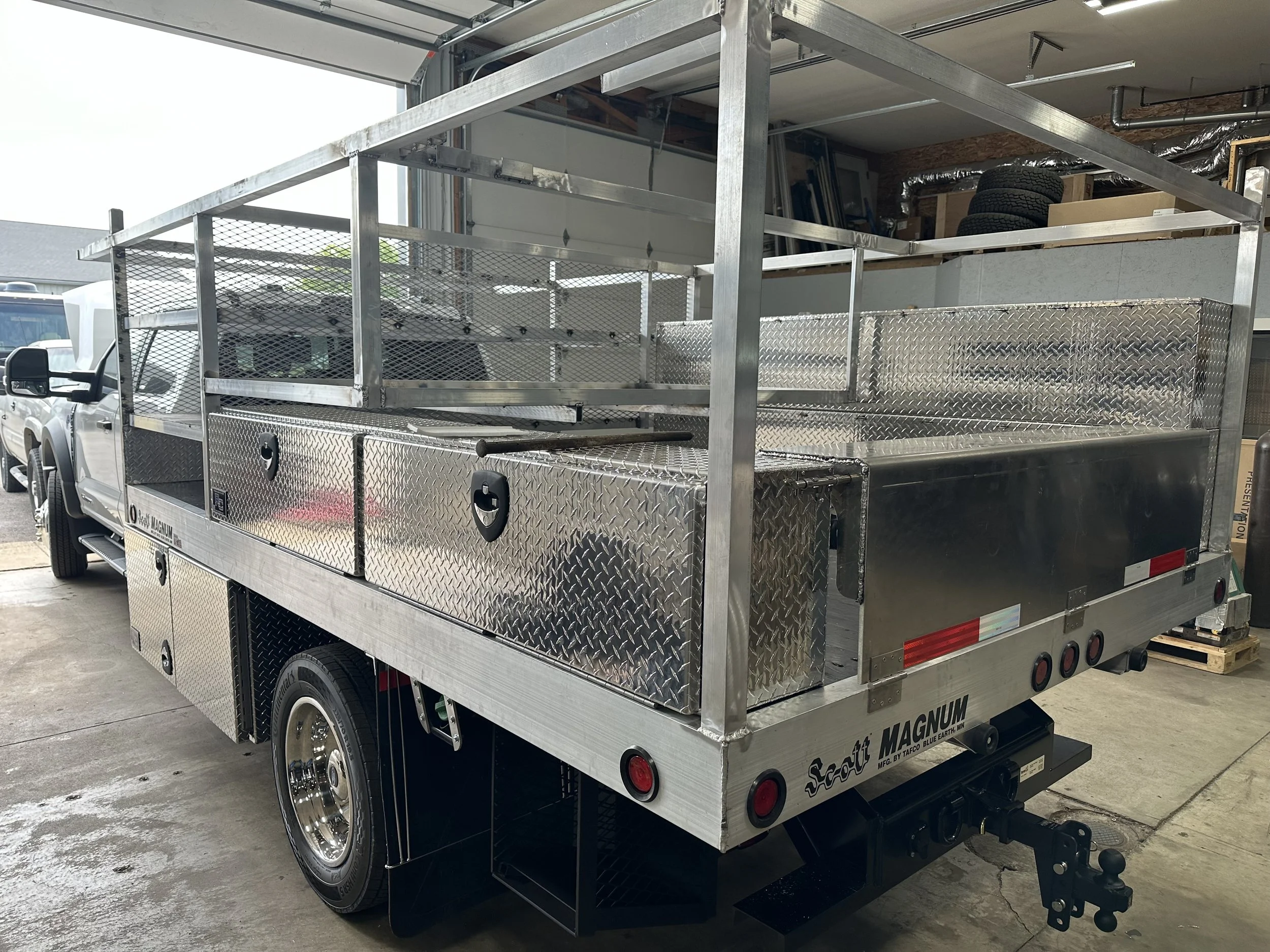 A silver Utility flatbed truck with storage compartments and open metal frame racks in a garage or workshop.