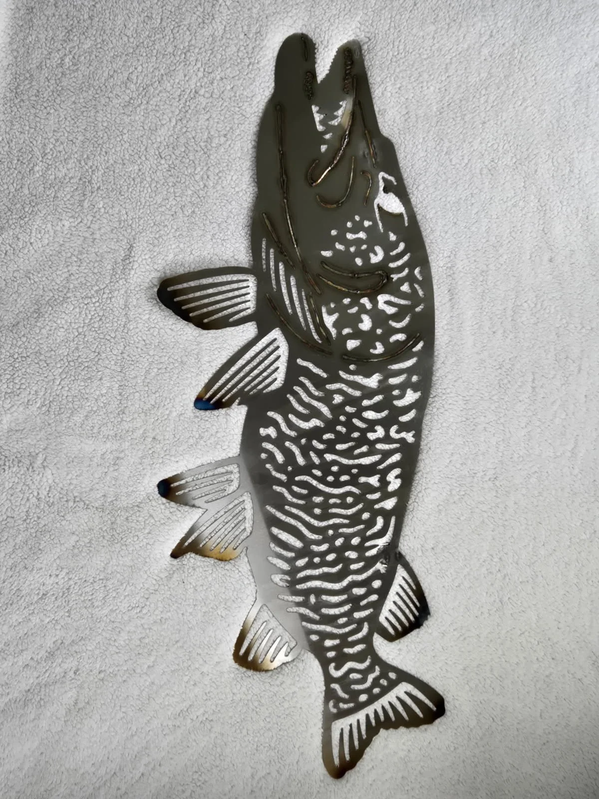 stainless steel Muskie, with cutout details, on a textured white background.