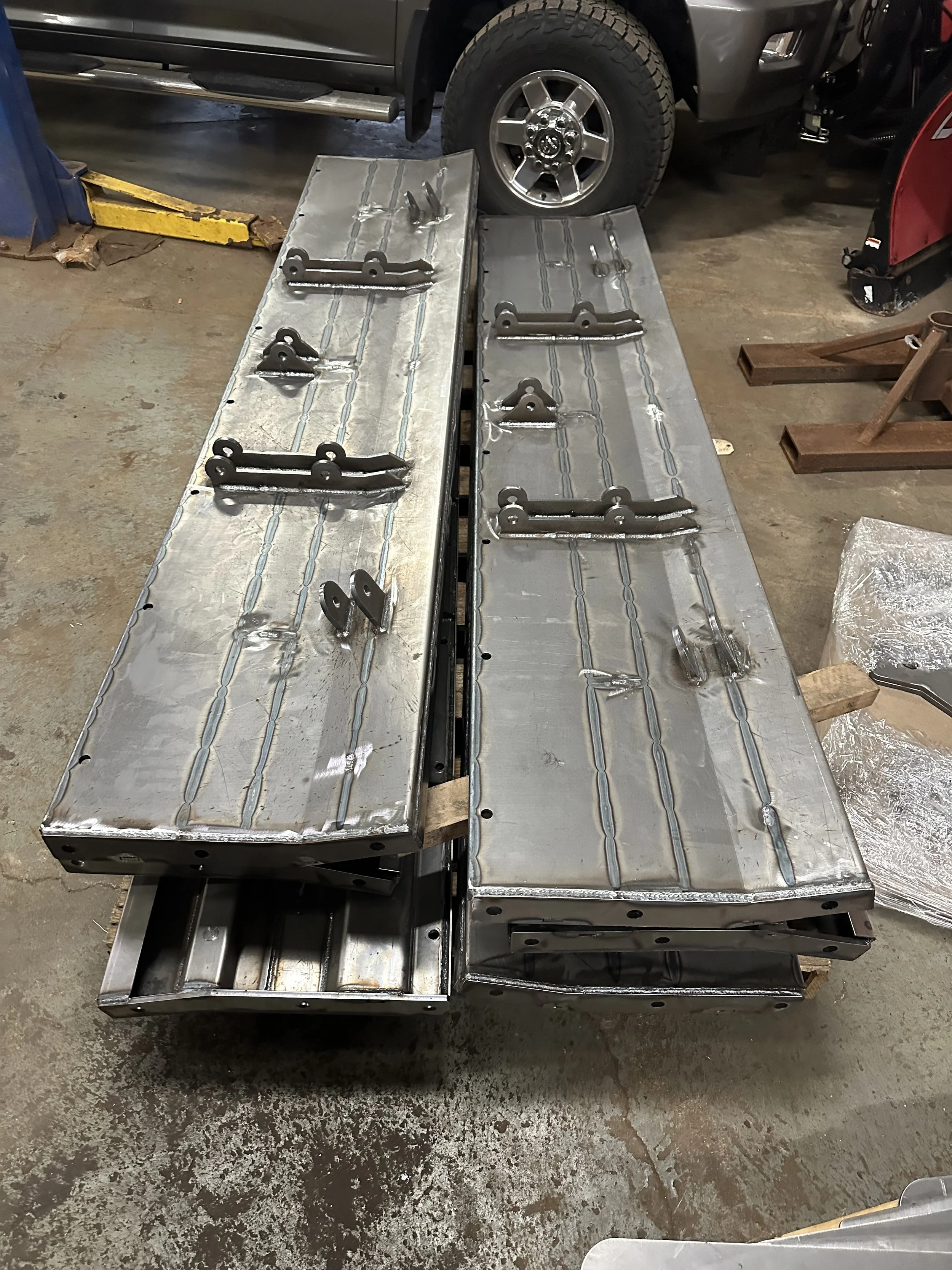 Two metal benches with black metal parts attached on top, located inside a garage or workshop, with a vehicle in the background.