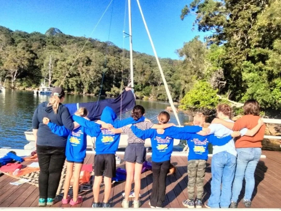 a group of leaders and kids on a camp standing with their backs to camera and arms around each other