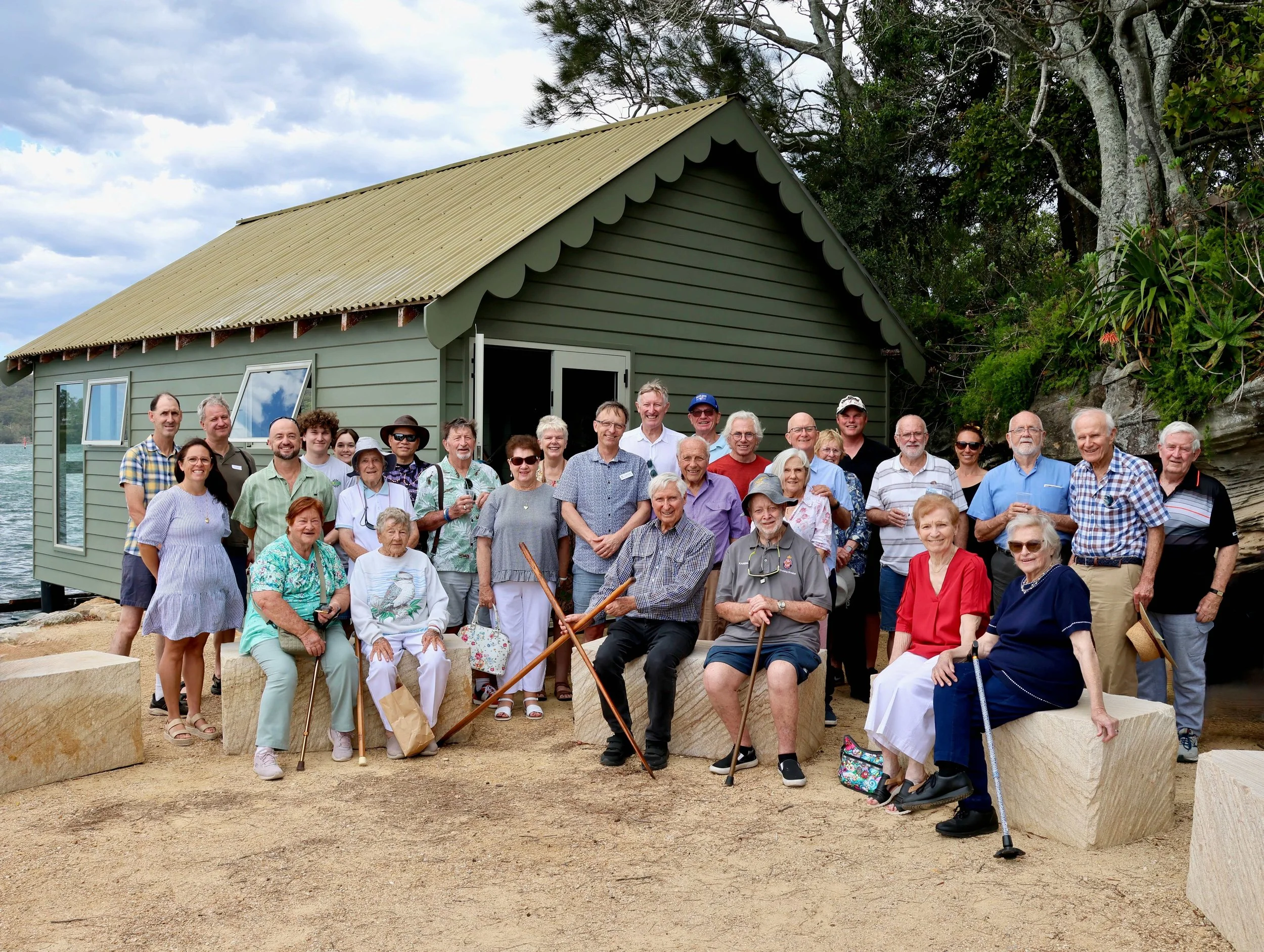 A group of around 20 people in front of a refurbished boat shed