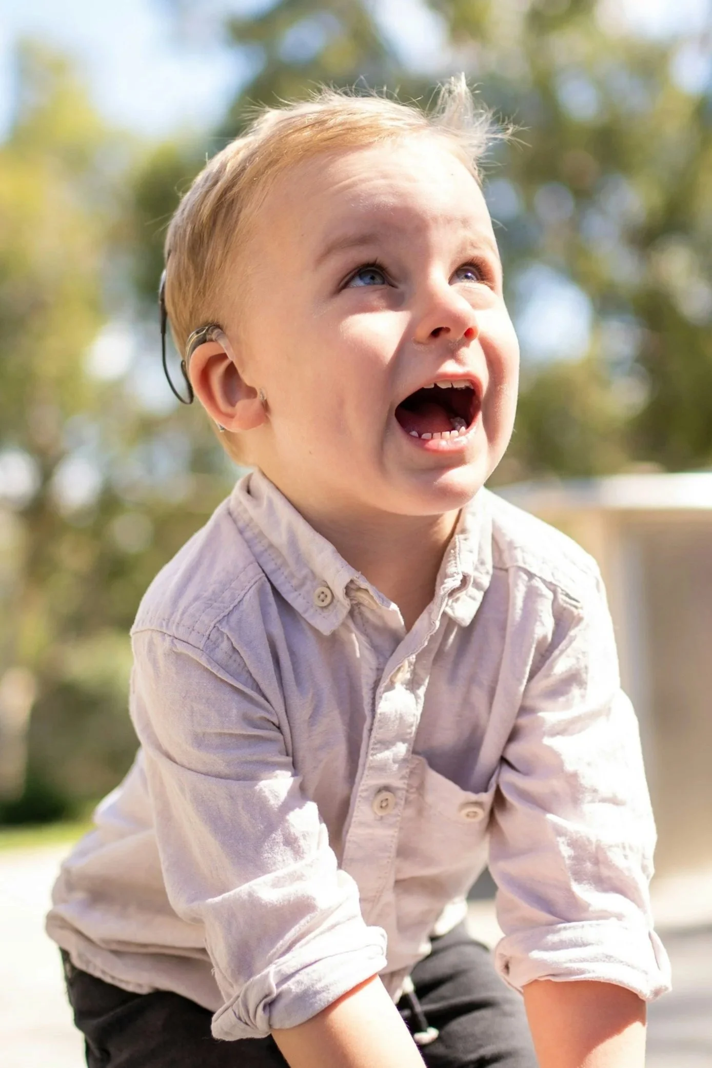 A young boy with a hearing aid is looking excitedly at the photographer