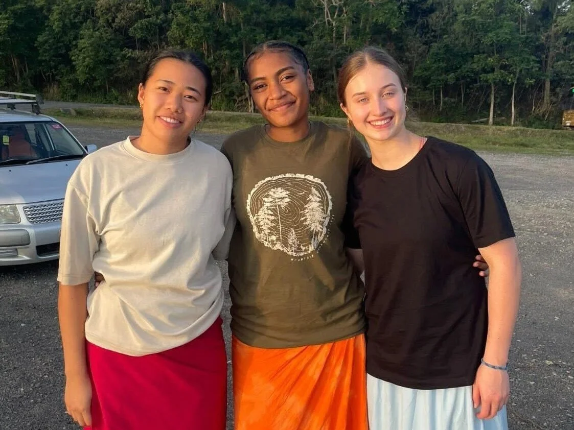 Three young women stand together smiling at the camera