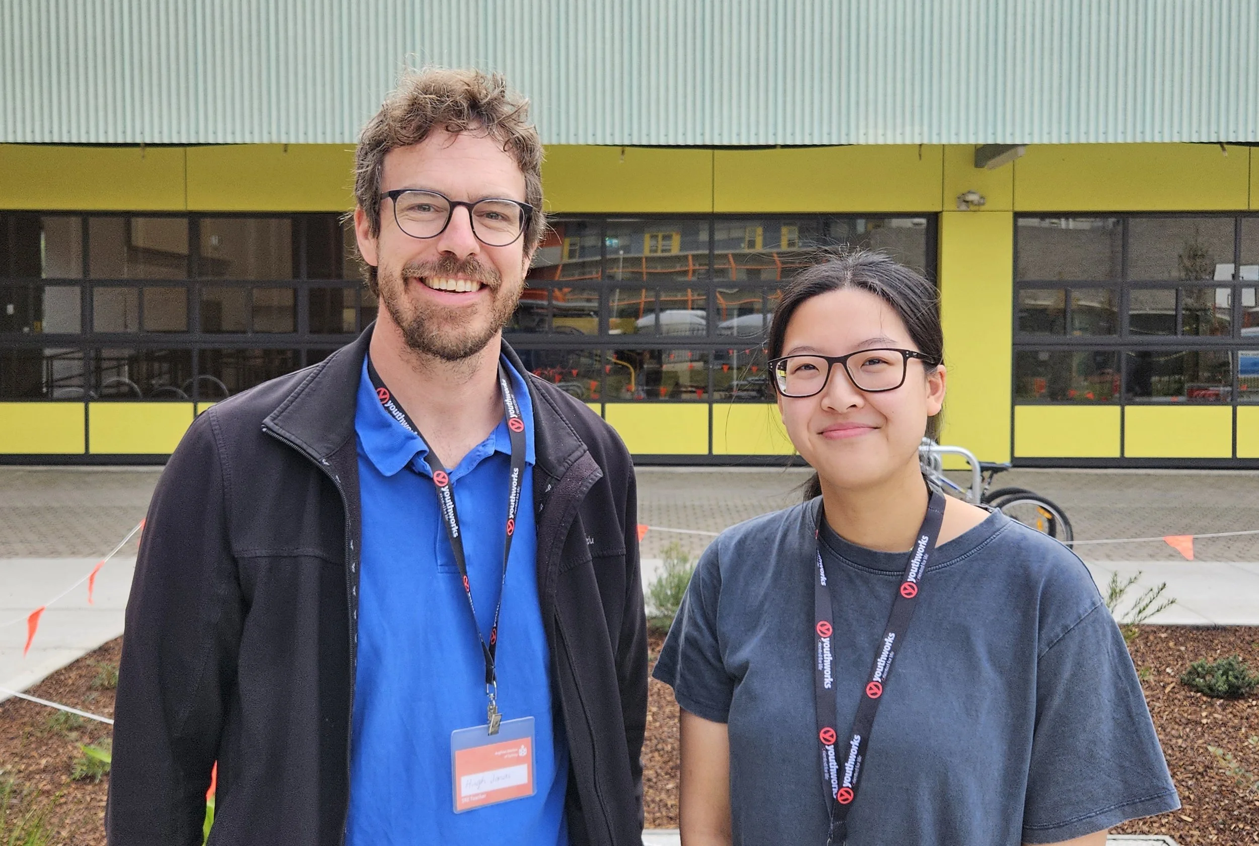 A man and a young woman stand together in front of a school