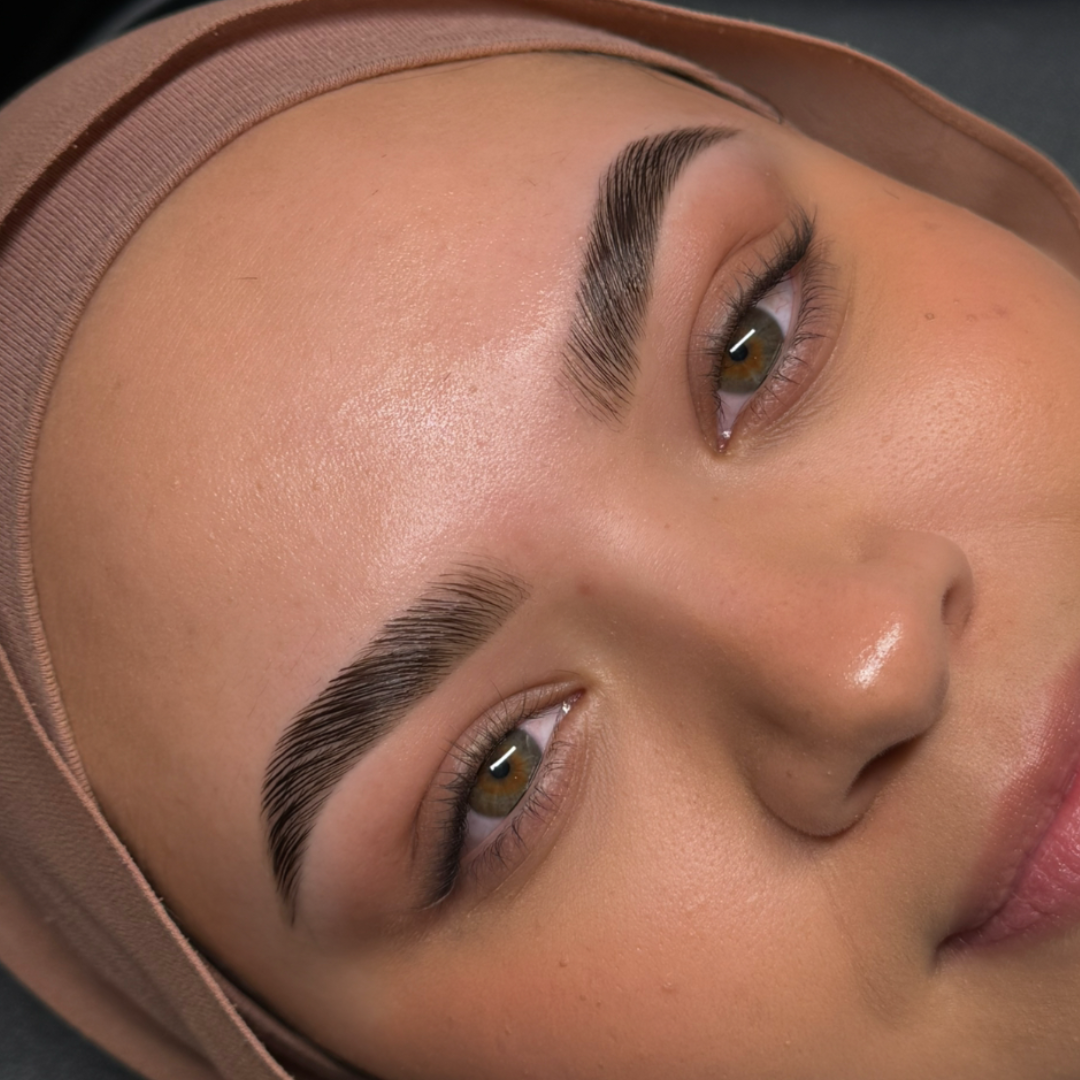 Close-up of a woman's face with well-groomed eyebrows, smooth skin, and a headscarf, lying on a black surface.
