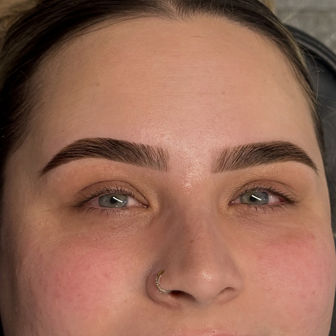 Close-up of a woman’s face focusing on her eyebrows, eyes, and nose, with visible light makeup and a gold nose ring.