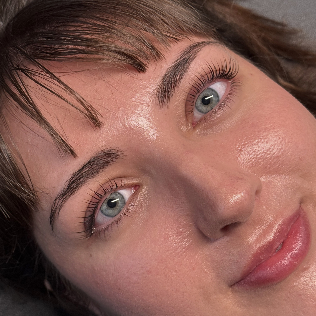 Close-up of a woman's face showing her blue eyes, brown eyebrows, and natural makeup with a focus on her skin and lashes.