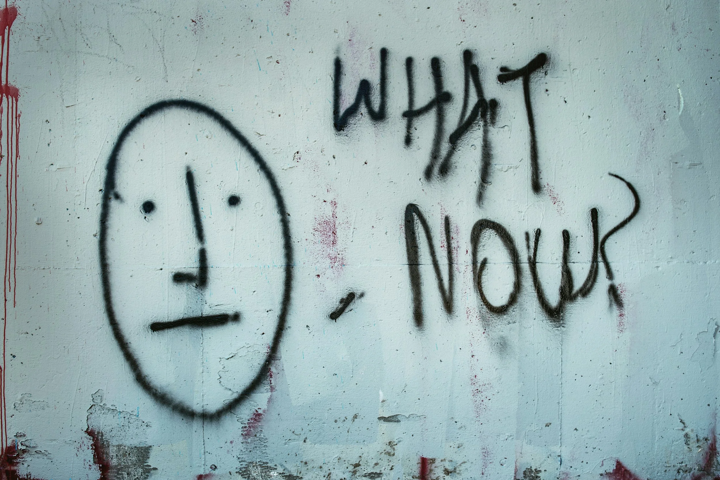 Graffiti saying "What now?" next to a drawn face with straight lips