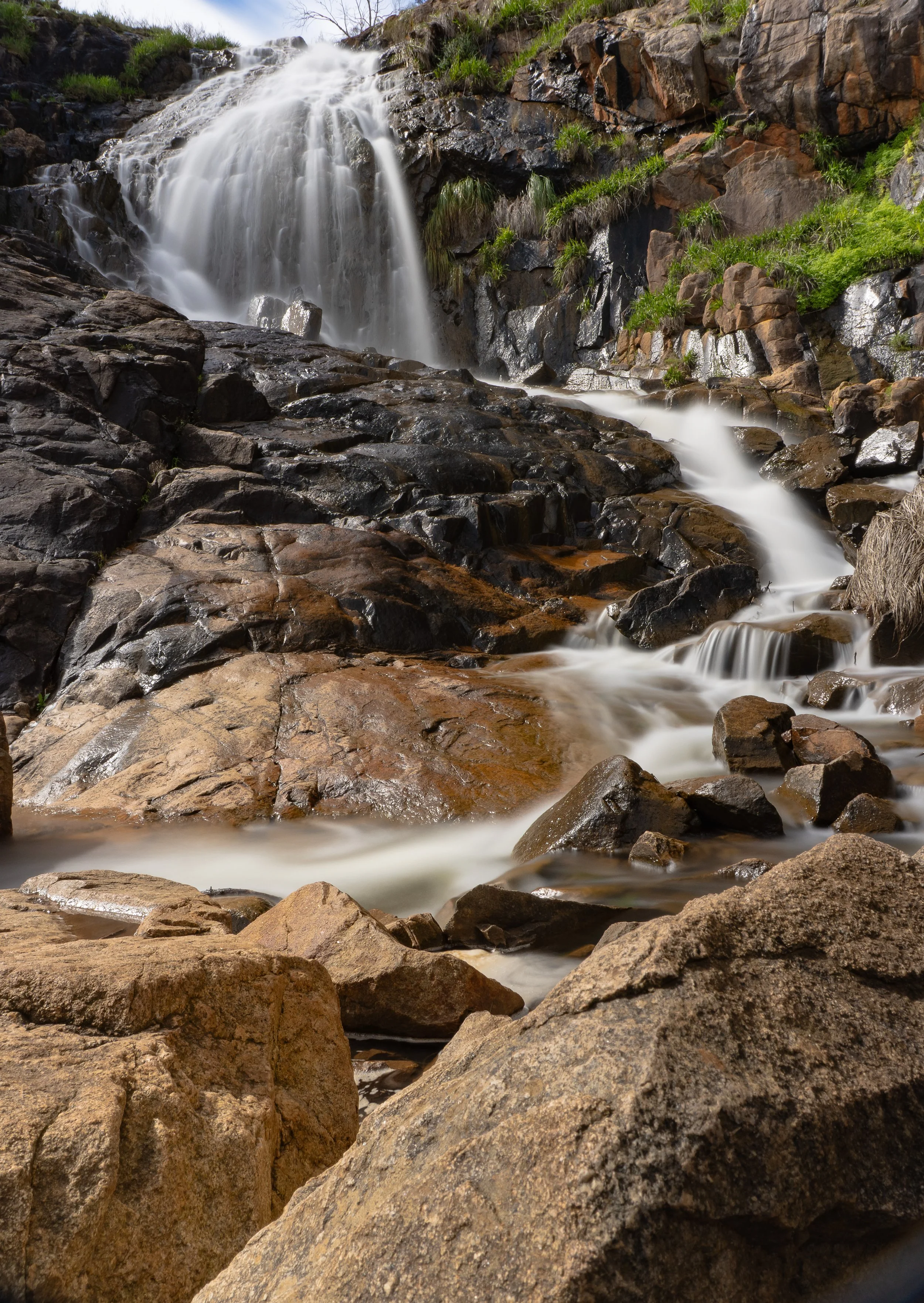A cascading waterfall flowing over rocks with lush green vegetation on the hillside.