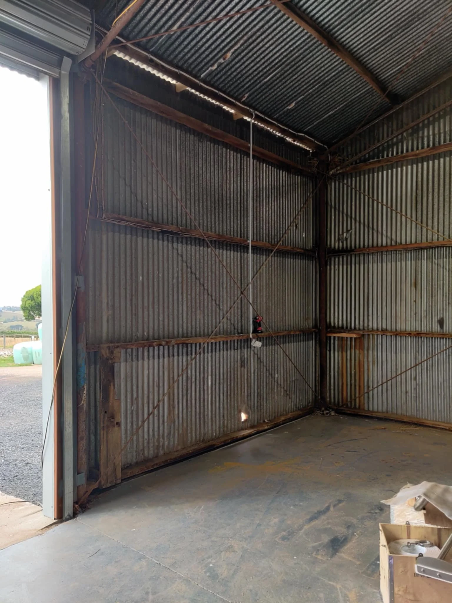 Interior of a partially constructed metal building with corrugated metal walls and a concrete floor. There is an open garage door on the left side, revealing the outdoors.