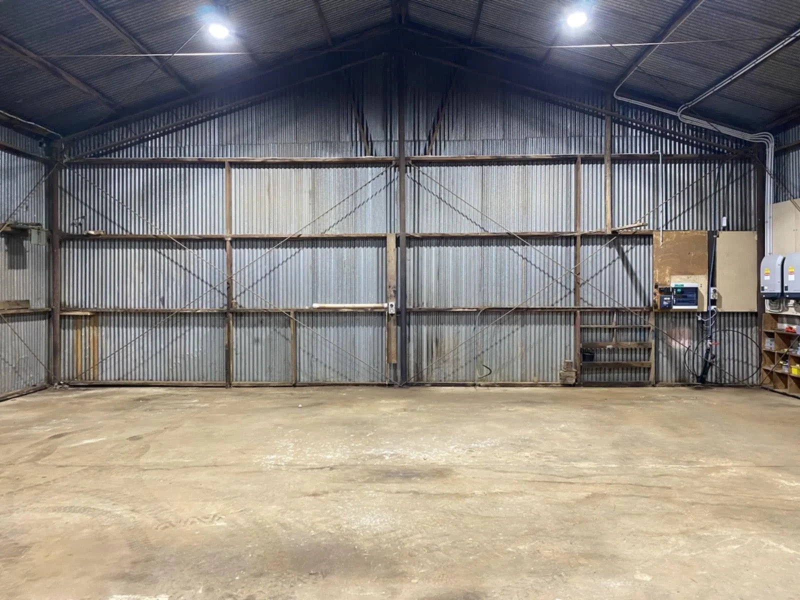 Empty industrial warehouse with metal paneled walls and ceiling, concrete floor, and electrical panels on the right wall.