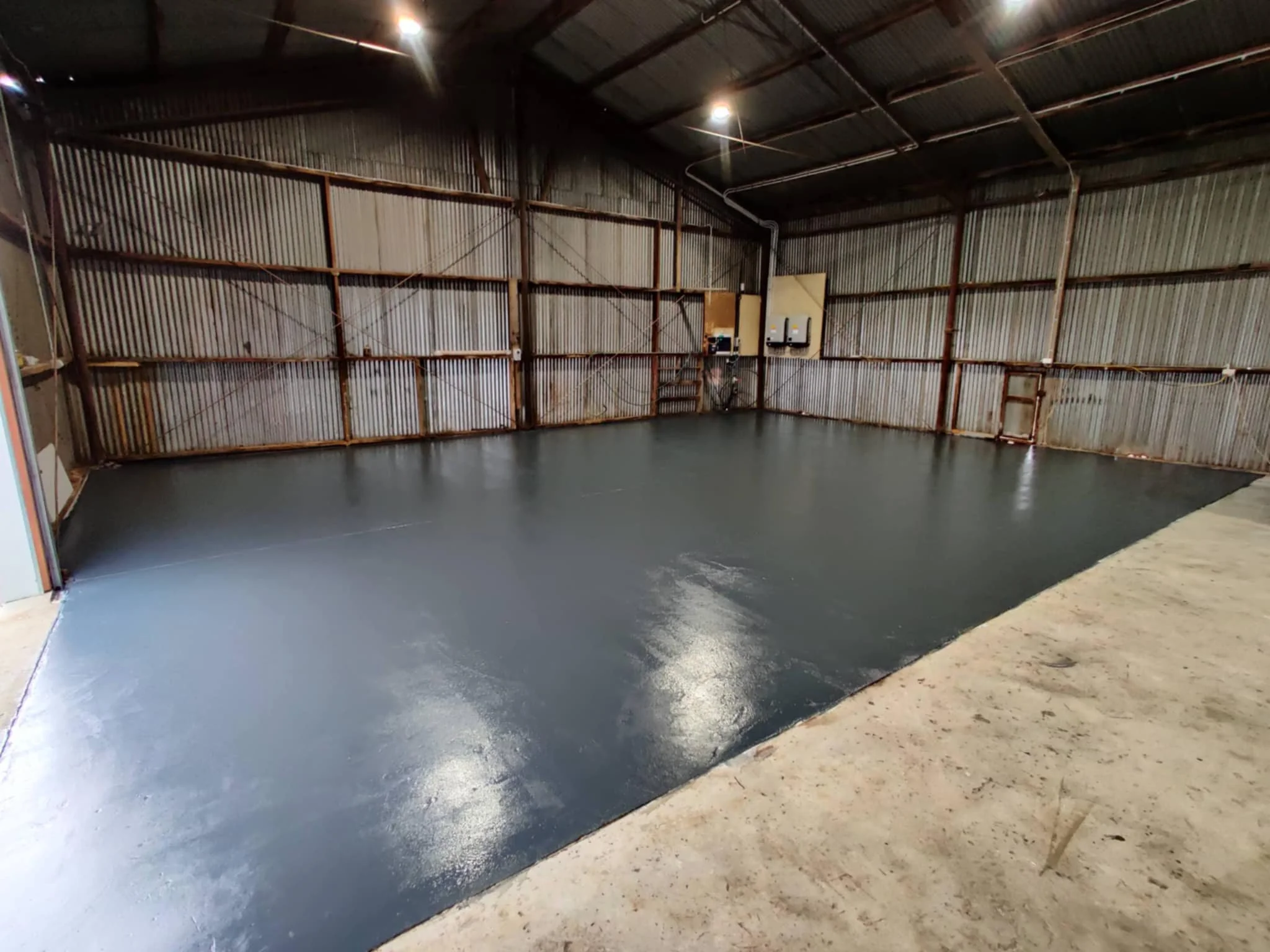 Empty industrial warehouse with newly coated black floor and corrugated metal walls.