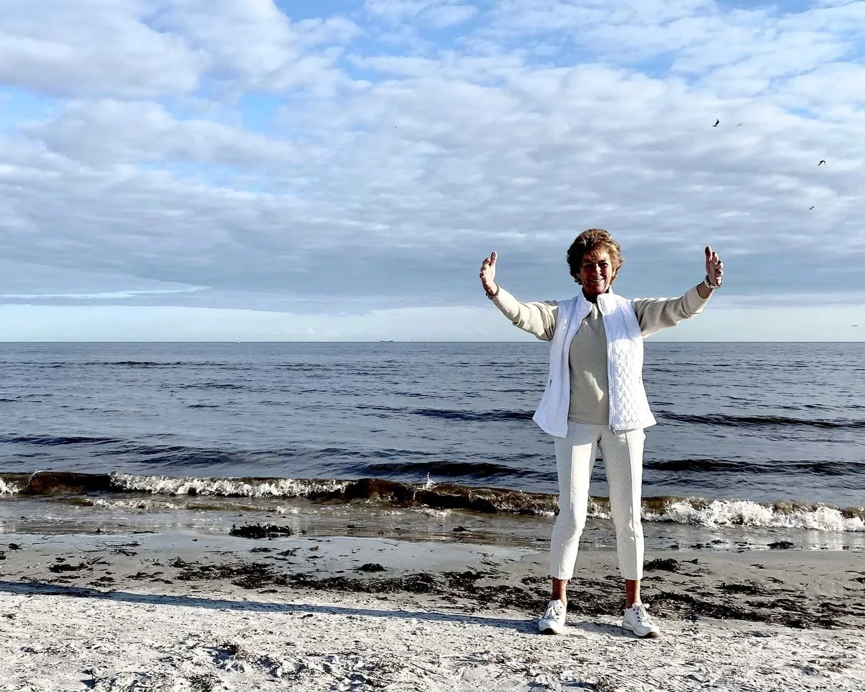 Yvonne håller ut armarna på en strand. Röstträning och coaching.