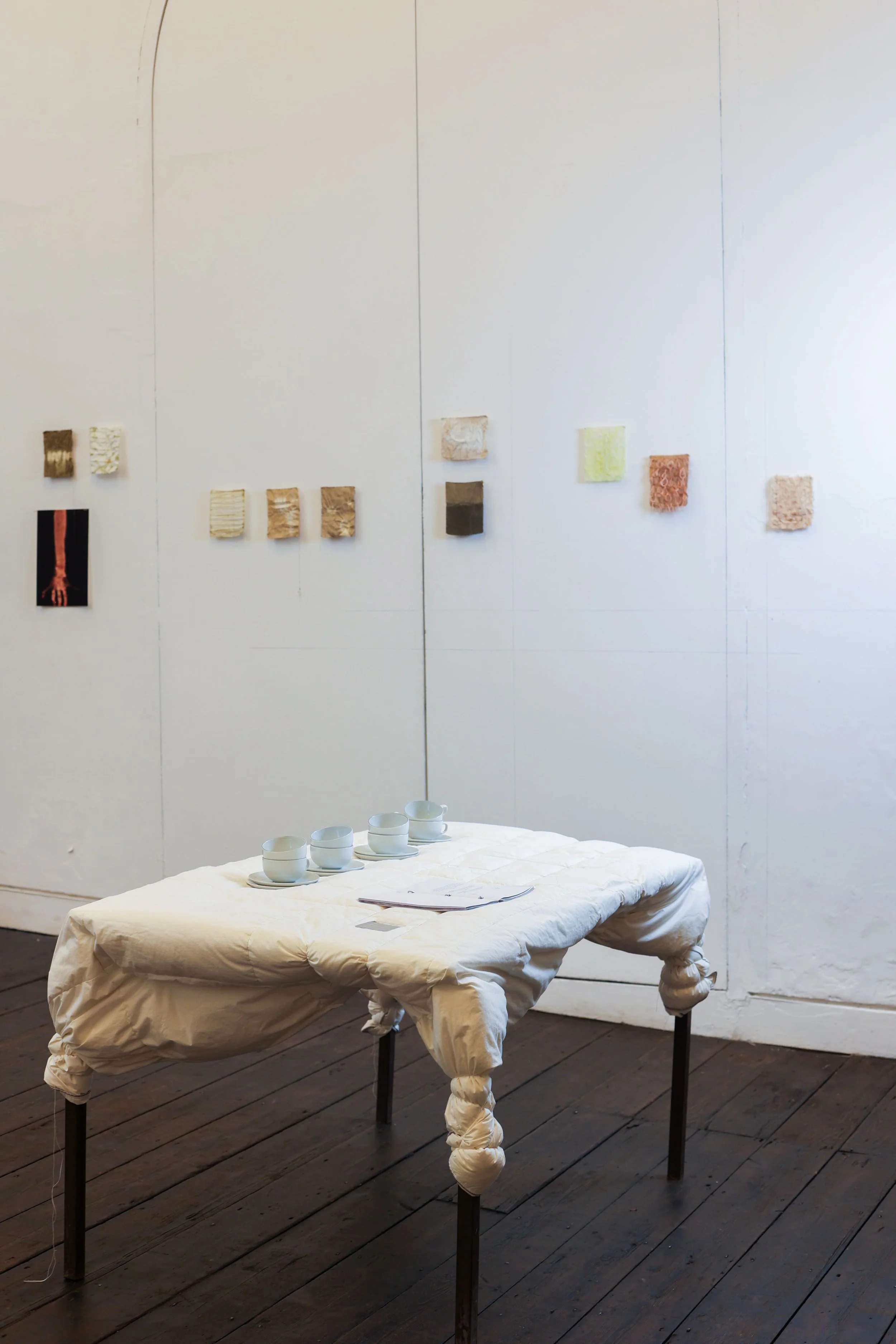 'Thin Skin, Thin Places', 2025.
Installation comprising a metal table, duvet, wire and thread; silk artworks dyed with rosemary pigment; herbal tea served in ceramic cups; and a publication bound with steel. Presented as part of 'Surfaced', Beaconsfi