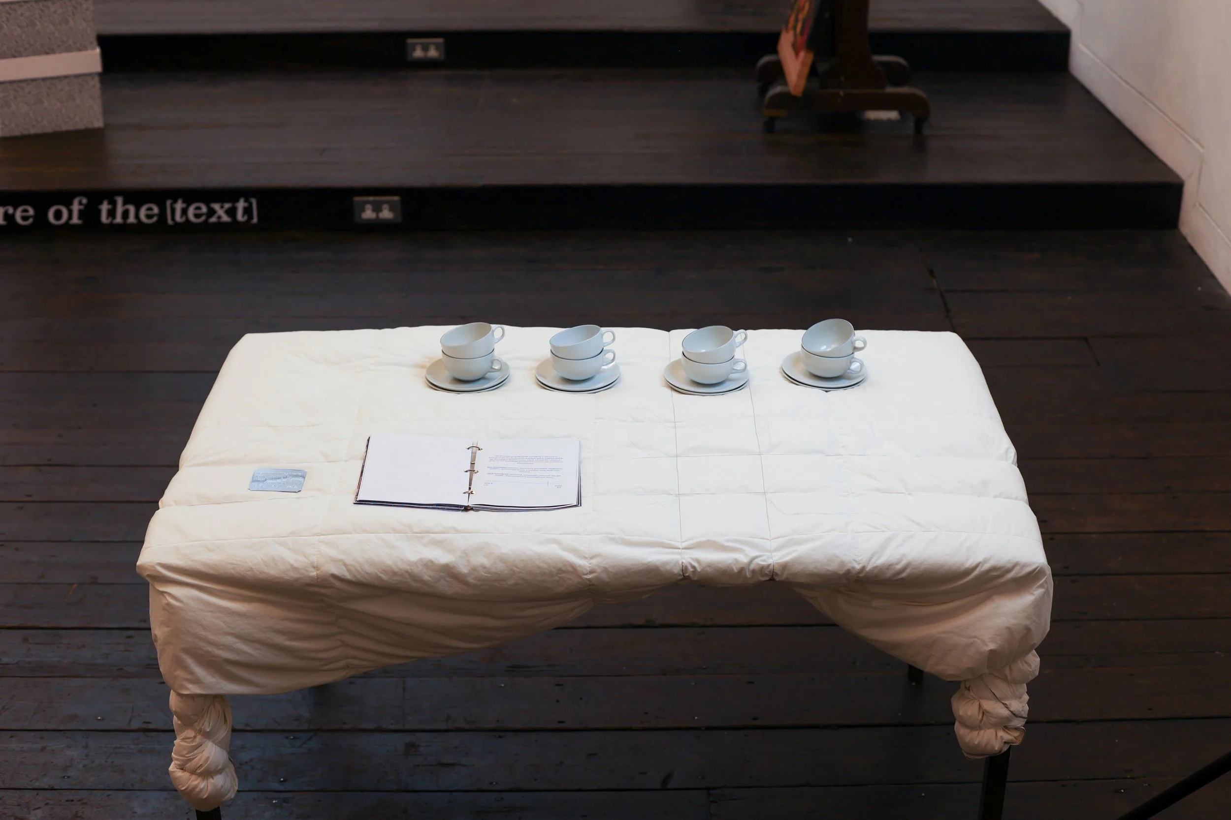 'Thin Skin, Thin Places', 2025. Installation comprising a metal table, duvet, wire and thread; silk artworks dyed with rosemary pigment; herbal tea served in ceramic cups; and a publication bound with steel. Presented as part of 'Surfaced', Beaconsfi