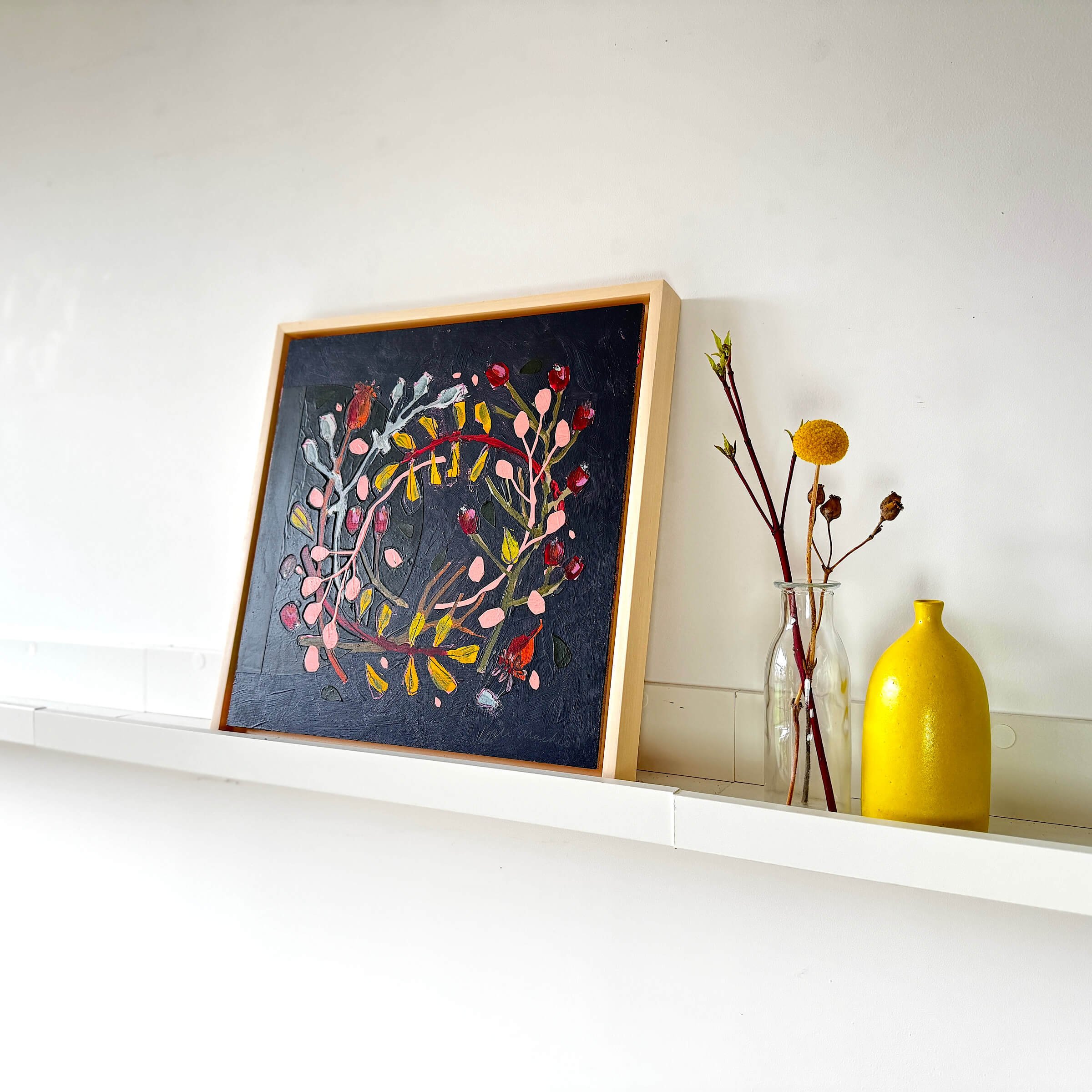 Wallis original mixed media botanical wreath painting by Ali Mackie displayed in a light wood tray frame on a white shelf.