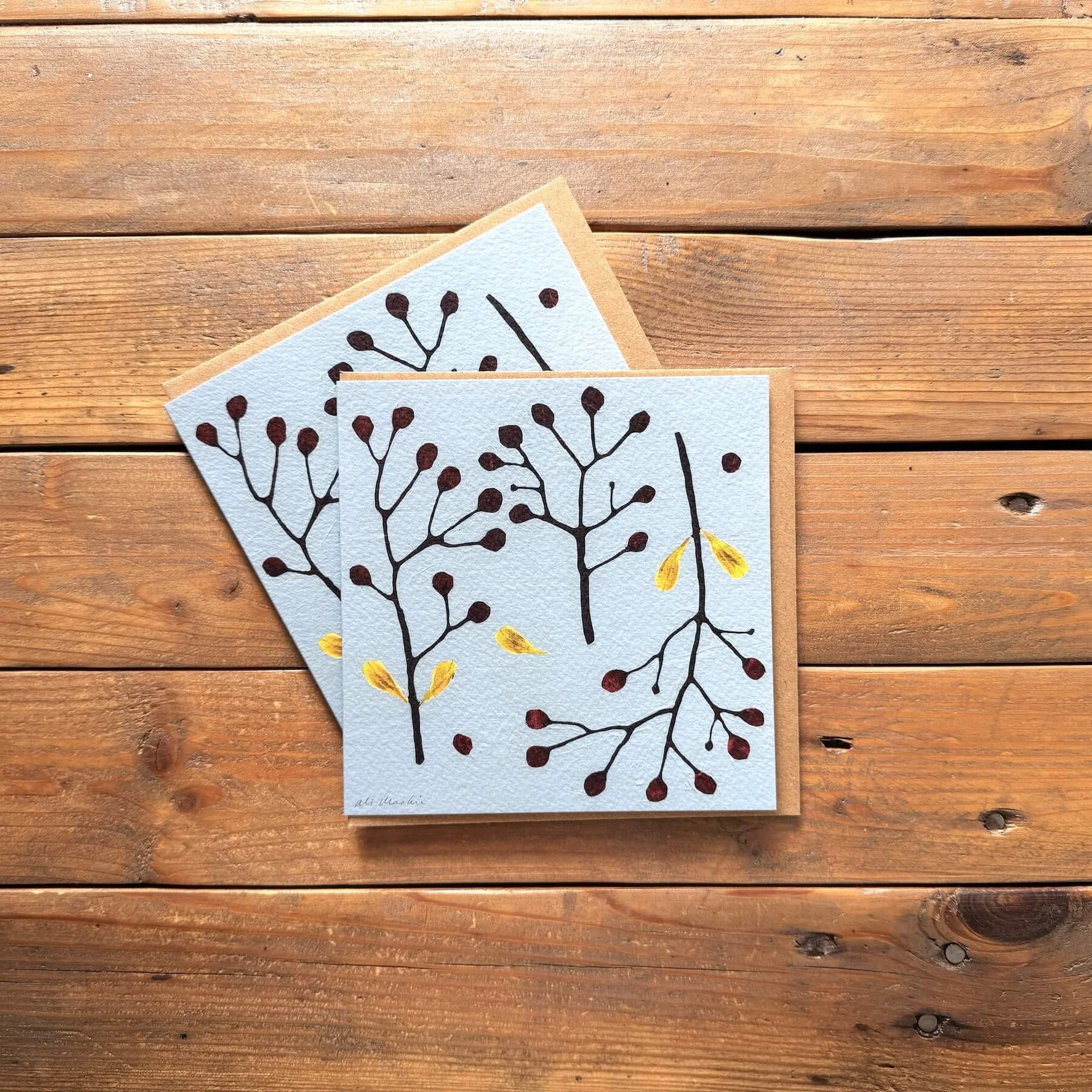 Pair of light blue festive botanical branch greeting cards with red berries and yellow leaves.